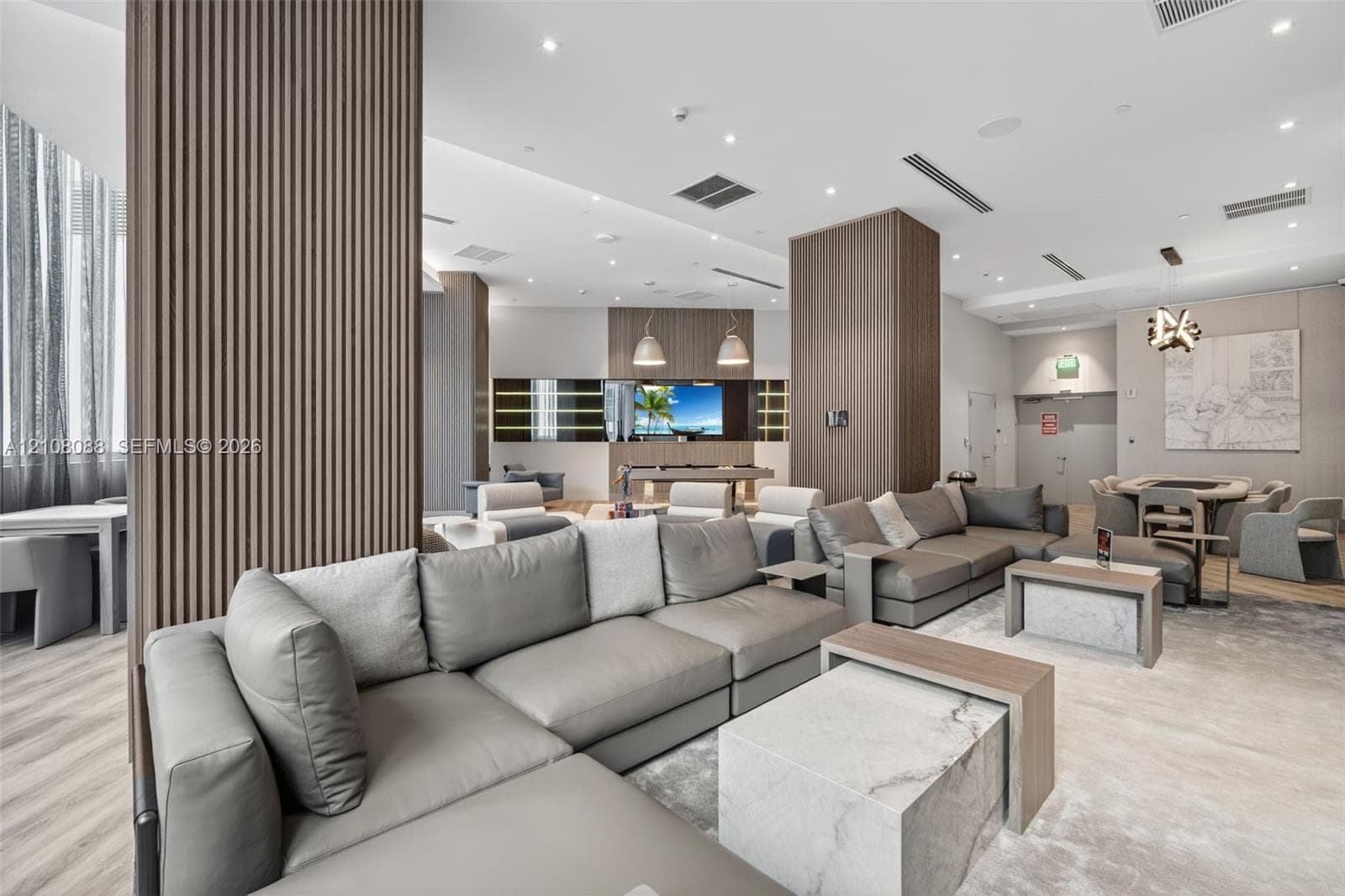 Open-concept lounge featuring wood-slat accent pillars, recessed ceiling lighting, light-toned wood-finish flooring, and floor-to-ceiling windows