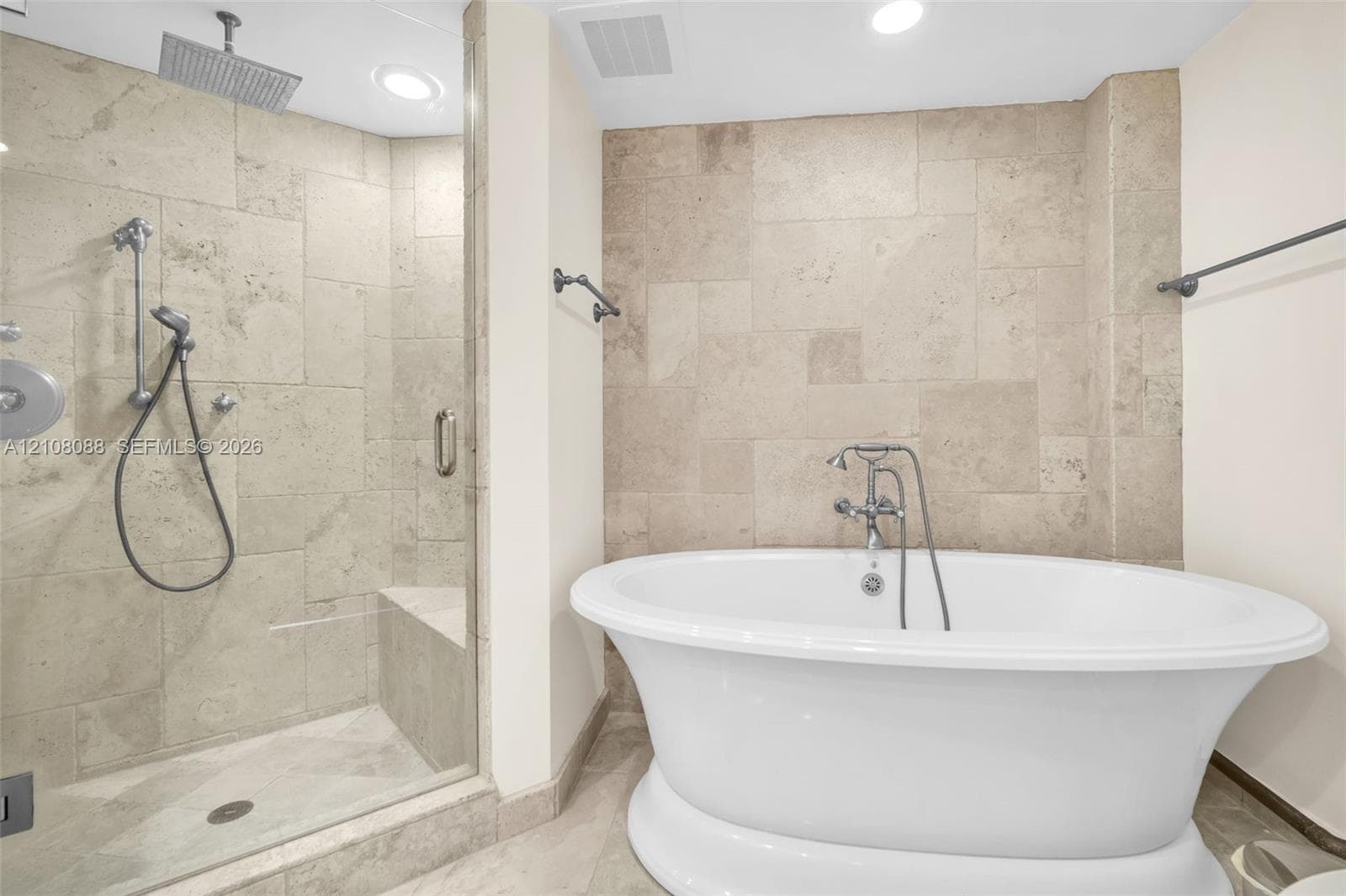 Freestanding soaking tub with chrome telephone-style faucet, glass-enclosed walk-in shower featuring a built-in bench, ceiling-mounted rainfall showerhead, and stone tile surround