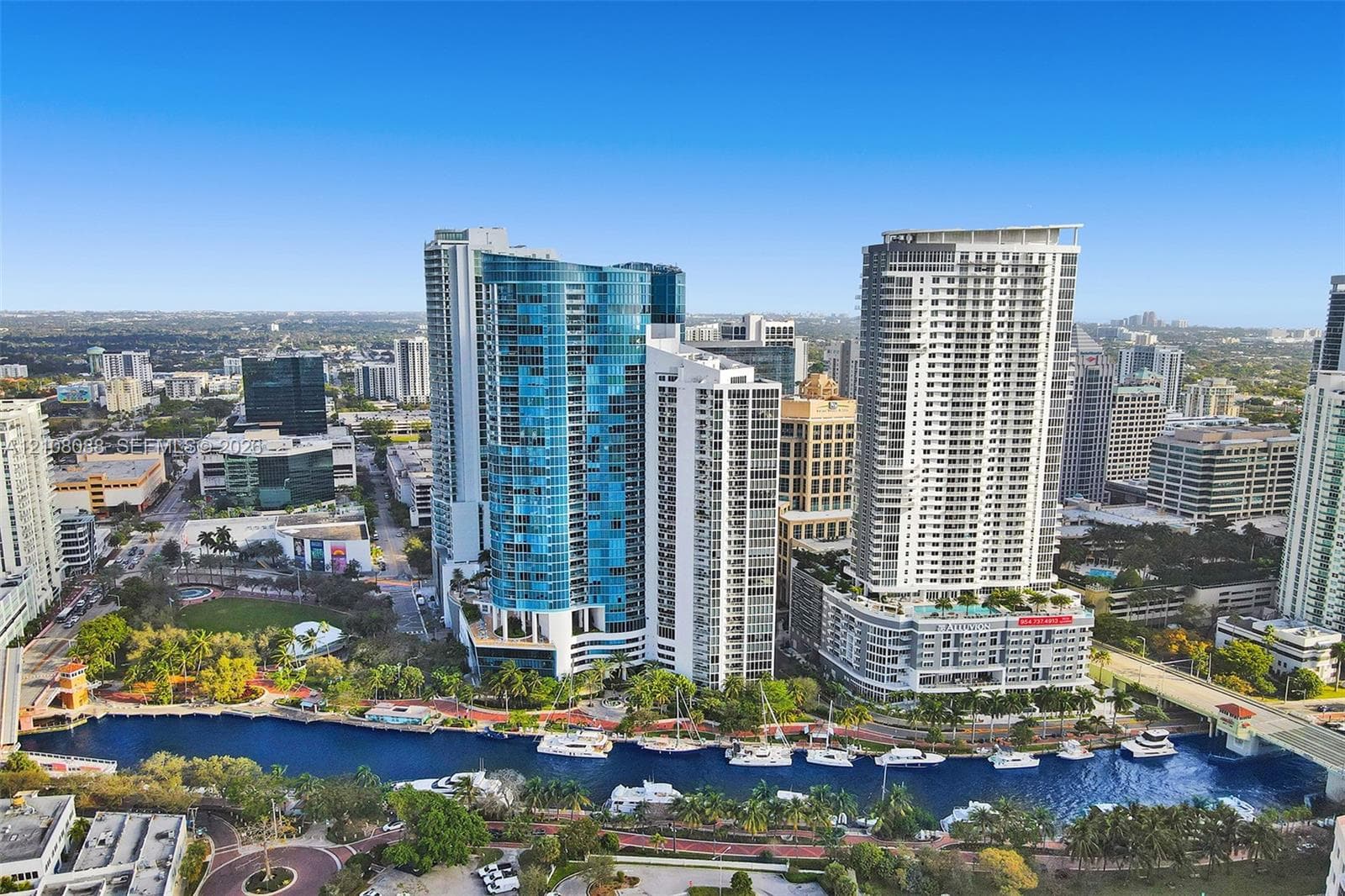 Aerial perspective featuring high-rise glass-clad architecture, a concrete waterfront promenade, and a deep-water canal supporting nautical traffic