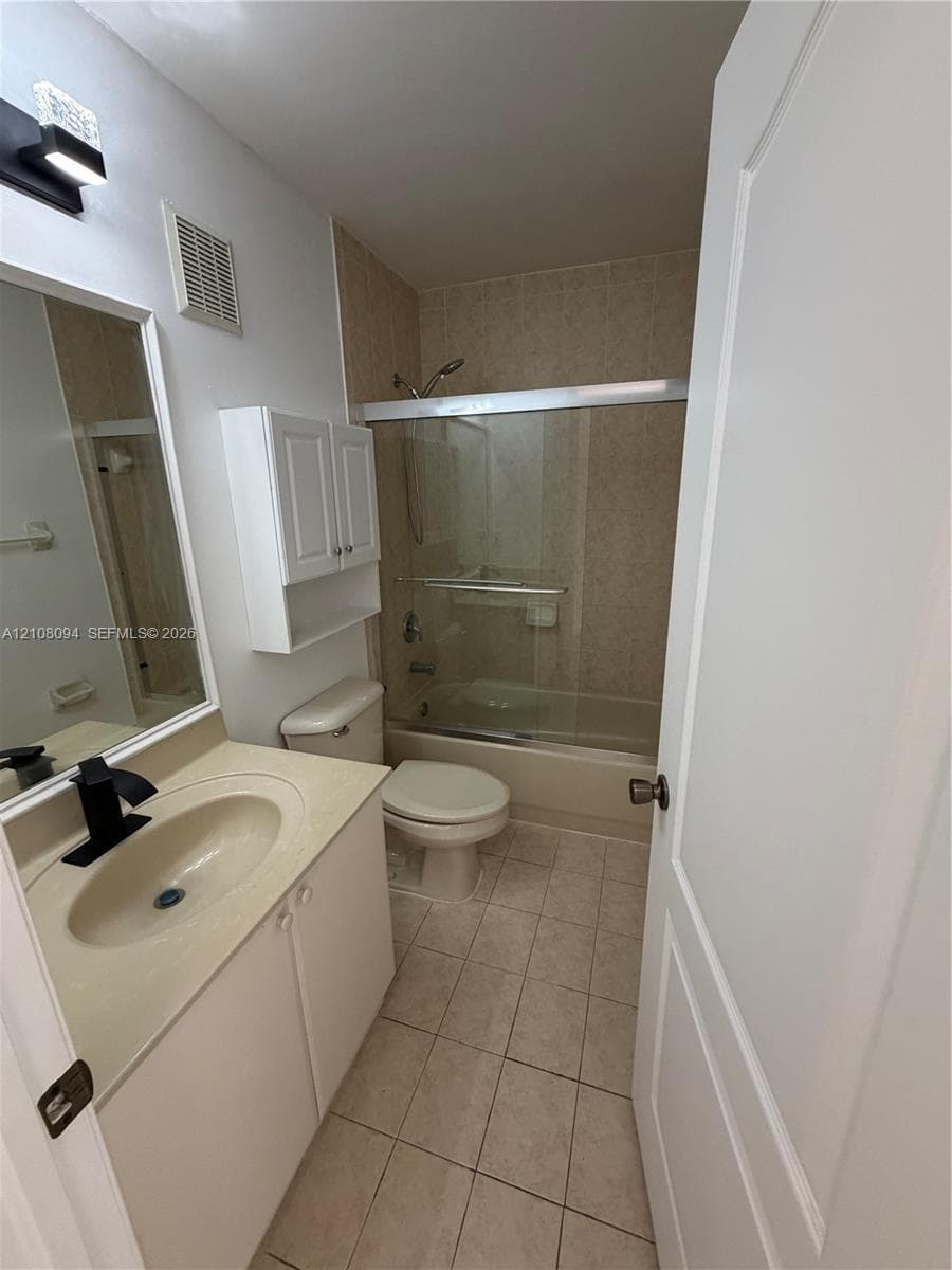 Bathroom featuring a vanity with a solid-surface countertop, matte black faucet, wall-mounted storage cabinet, and a tiled shower surround with a glass enclosure