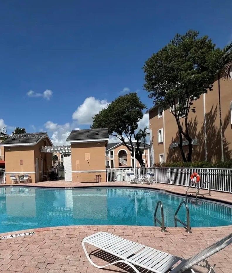 Swimming pool with paver decking, metal perimeter fencing, and decorative pergola structure