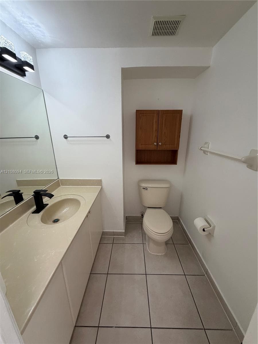 Countertop vanity with an integrated basin, matte black faucet, full-width mirror, tile flooring, and wall-mounted wood-finish cabinetry