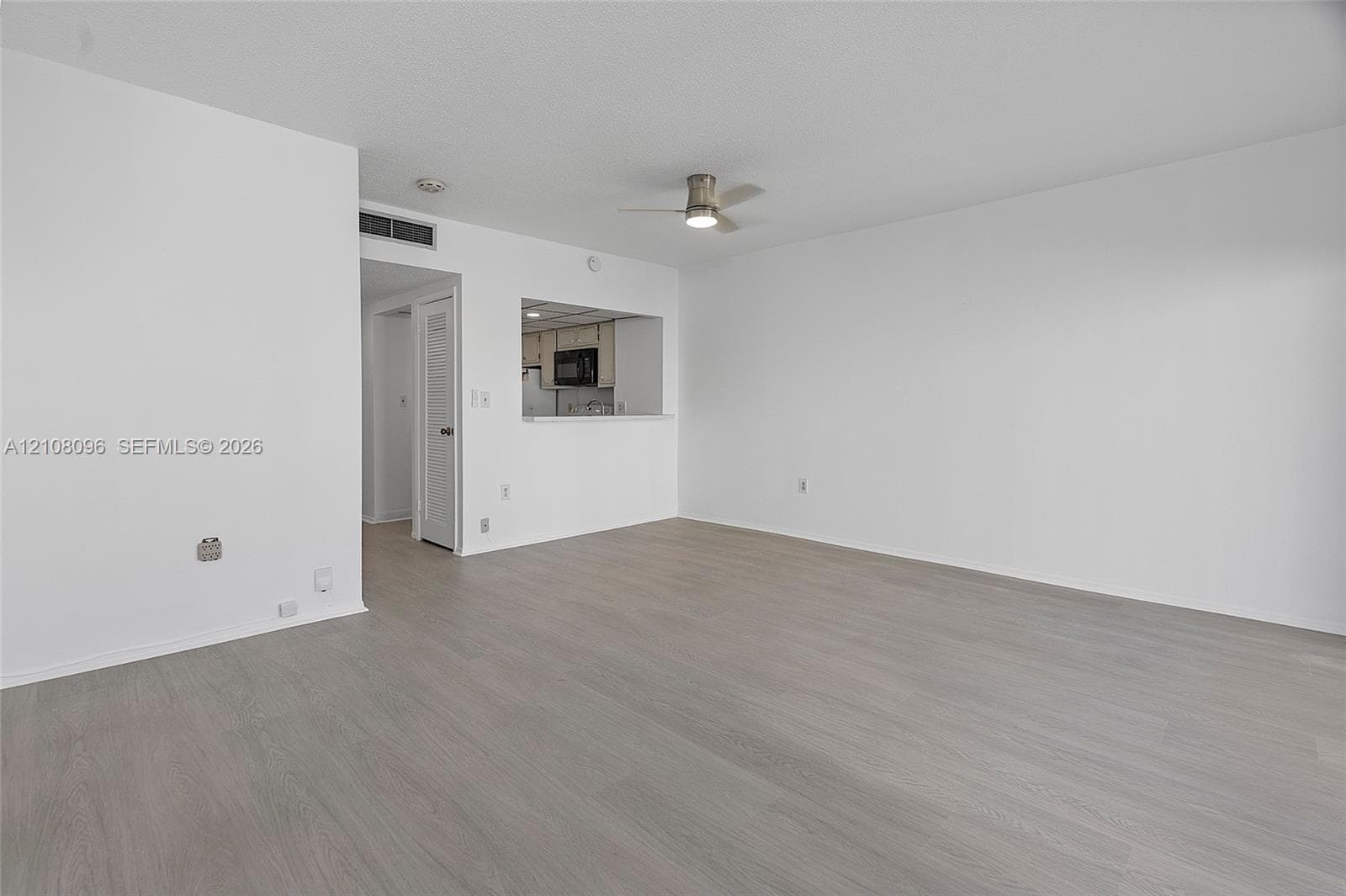 Open-concept interior featuring neutral wall tones, wood-finish flooring, a ceiling fan with integrated lighting, and a kitchen pass-through window
