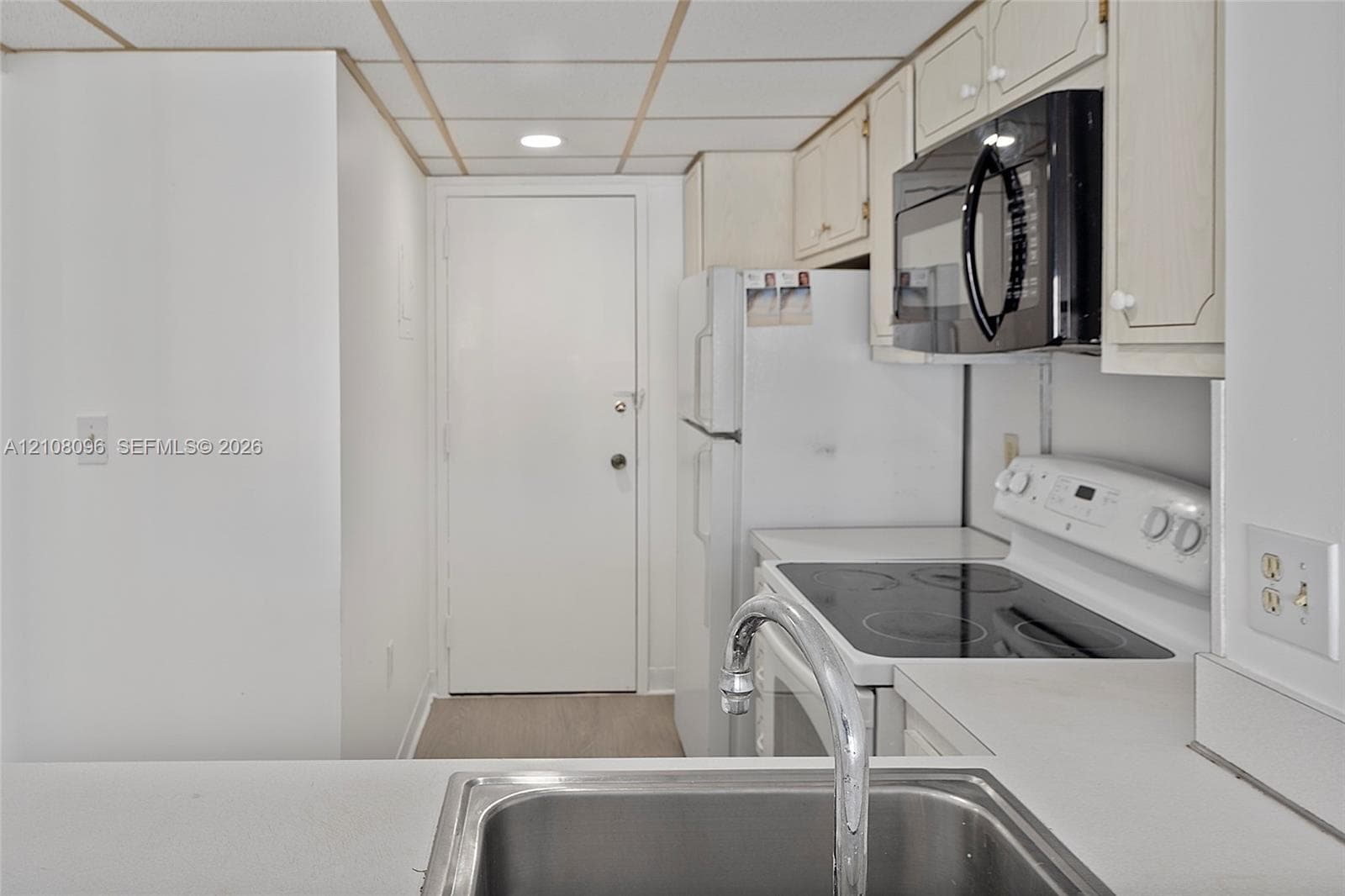 Kitchen featuring white cabinetry, an integrated microwave, a built-in electric range, and a stainless steel sink with a chrome faucet