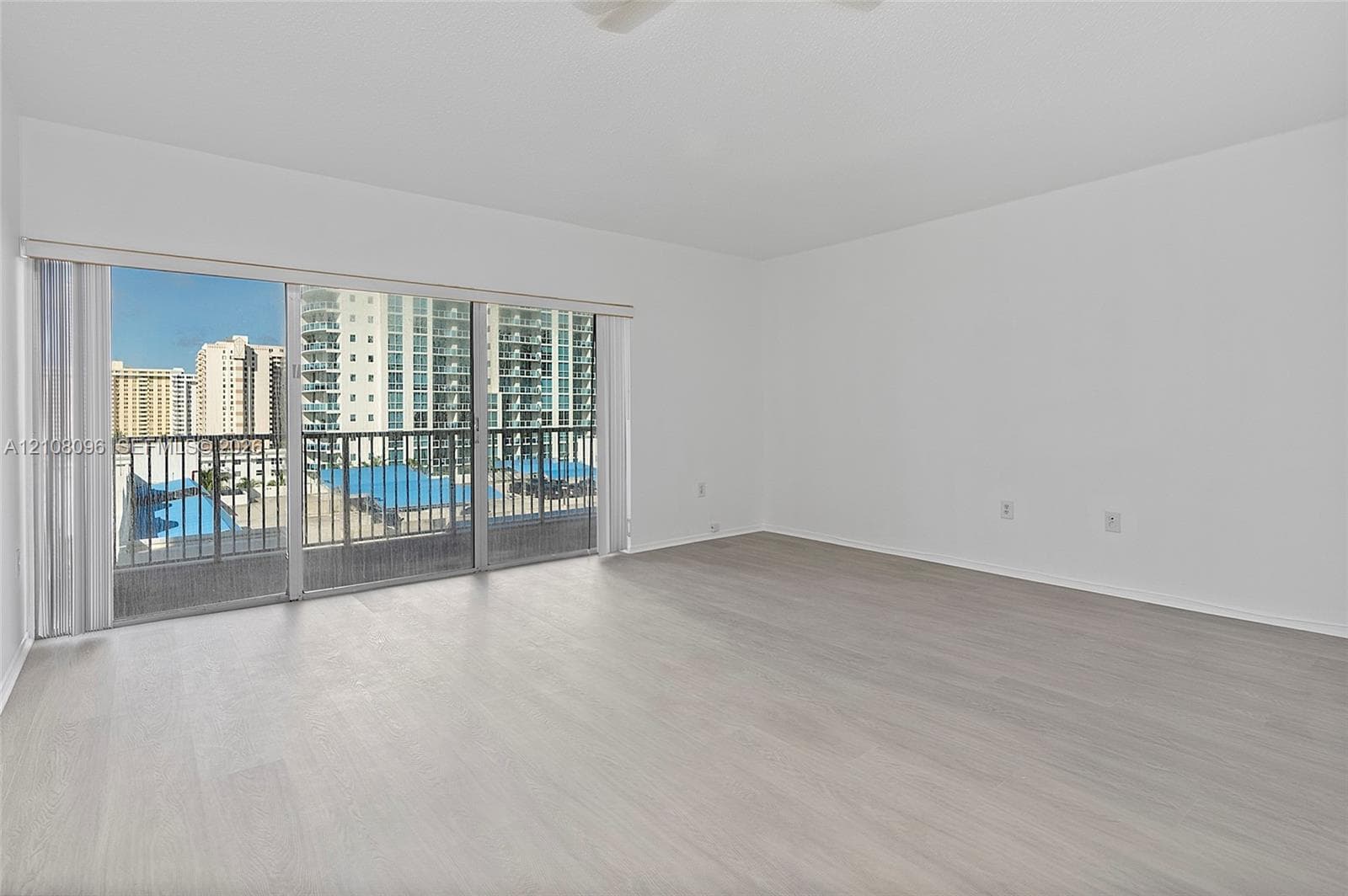 Open-concept interior featuring light wood-finish flooring, sliding glass balcony doors, and a metal-railed balcony