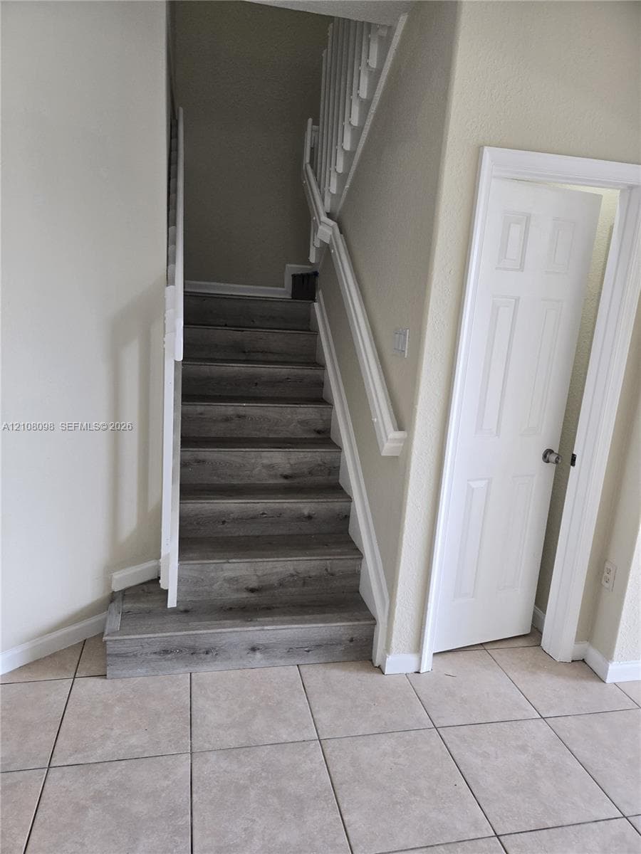 Staircase featuring wood-finish treads and white painted handrails, complemented by large-format ceramic tile flooring and a multi-panel interior door