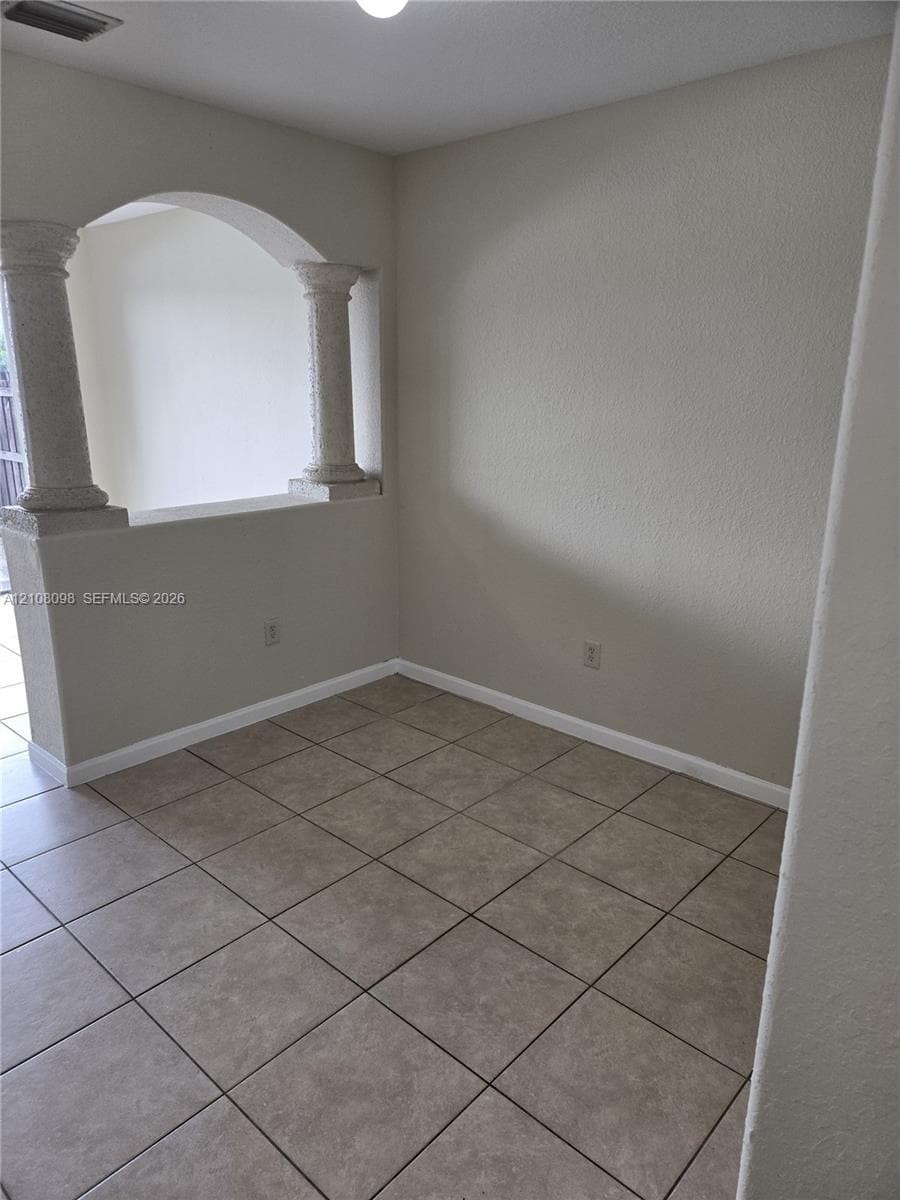 Interior space featuring ceramic tile flooring, a half-wall partition, and two decorative architectural columns supporting an arched overhead cutout