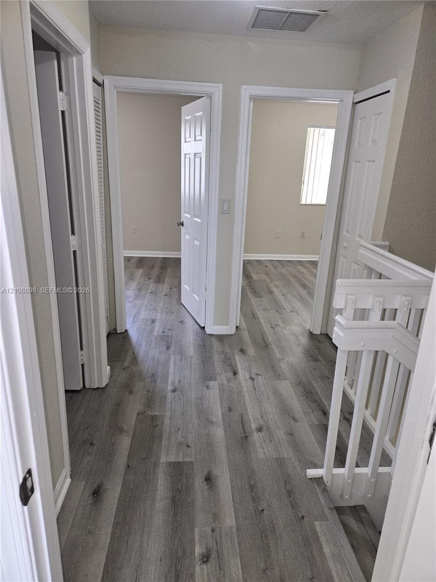 Hallway featuring wood-finish flooring, white paneled interior doors, and a painted wood staircase railing