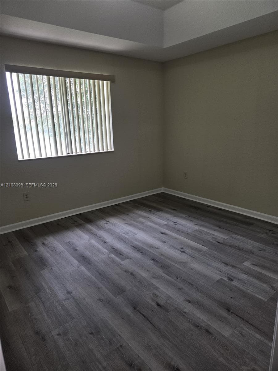 Room featuring wood-finish flooring, a tray ceiling, and a single window with vertical blinds