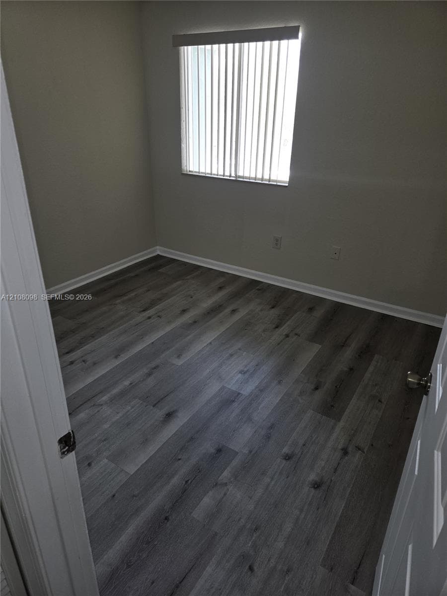 Room featuring wood-finish flooring, neutral wall paint, and a window with vertical blinds