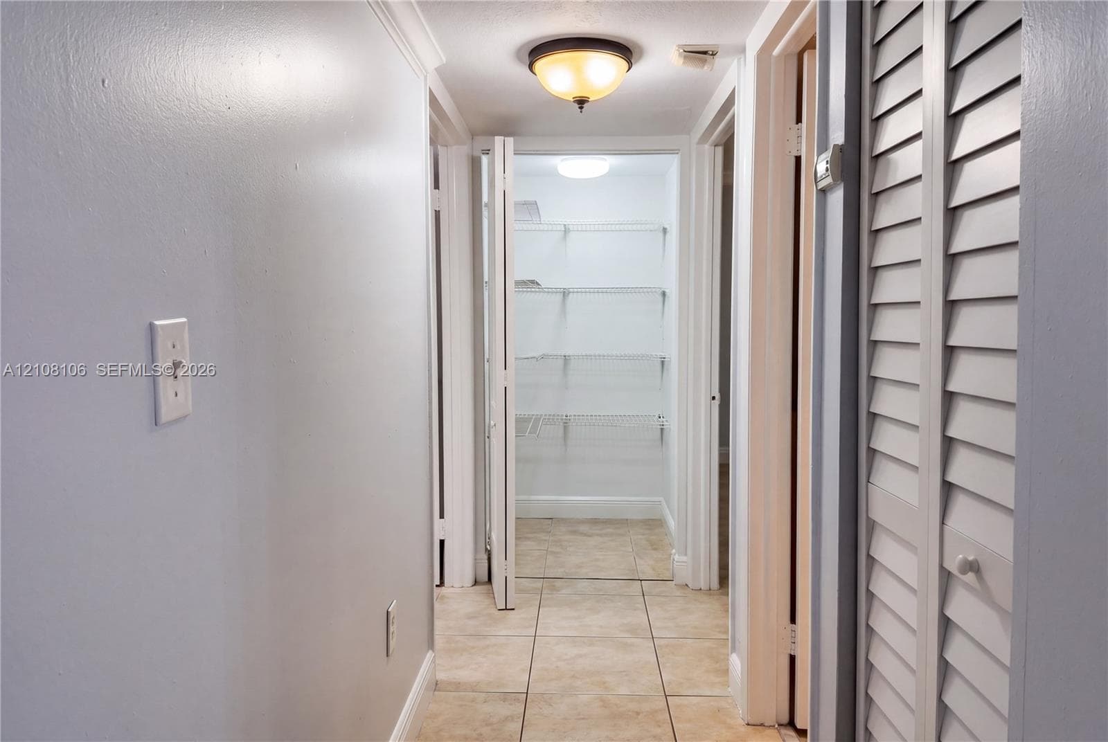 Hallway featuring tile flooring, louvered bi-fold closet doors, and walk-in pantry storage with integrated wire shelving