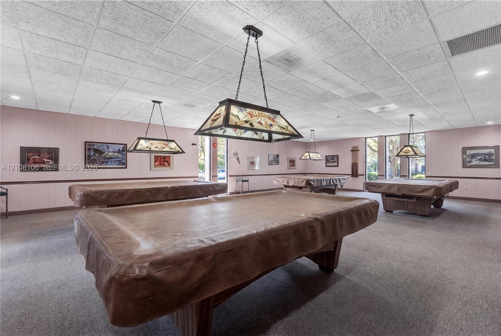 Spacious recreation room featuring a drop ceiling with recessed lighting, wall-to-wall carpeting, and multiple custom pendant fixtures with stained-glass accents