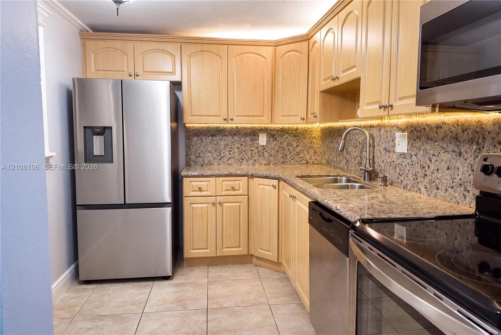 Kitchen featuring light-finish cabinetry, stone-texture countertops, stainless steel appliances, under-cabinet lighting, and tile flooring