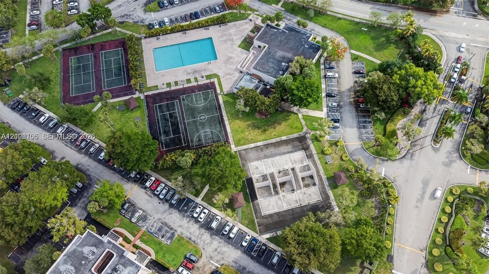 Community amenities including a swimming pool, two tennis courts, and a basketball court, set within a landscaped site featuring mature trees and paved parking areas
