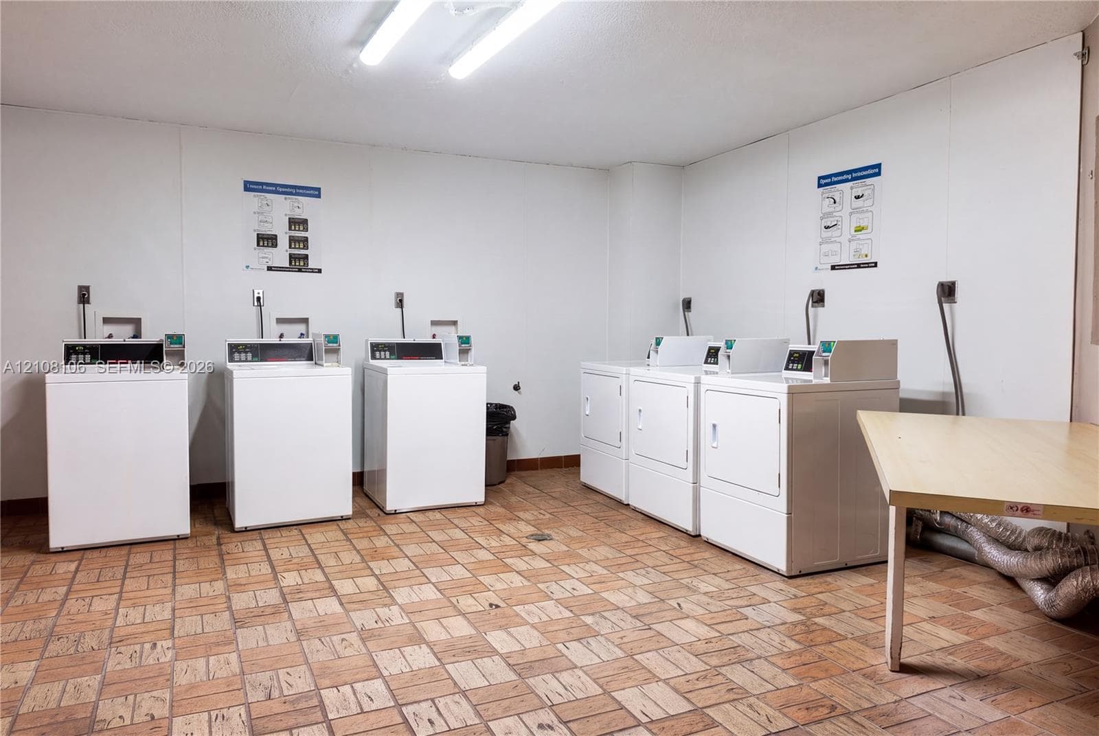 Laundry room featuring six coin-operated appliances, tile flooring, and a dedicated folding surface