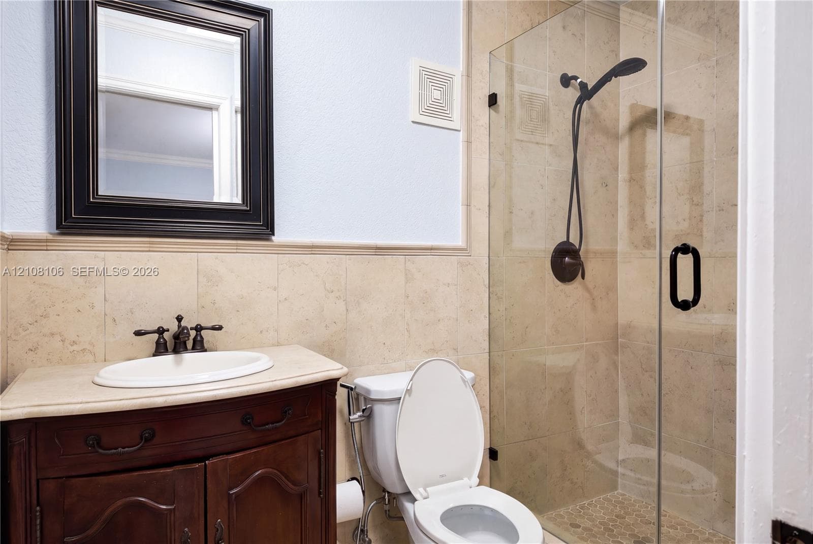 Bathroom featuring a dark wood vanity with a light-toned countertop, oval undermount sink, oil-rubbed bronze faucet, and walk-in shower with a frameless glass door and stone-tile surround