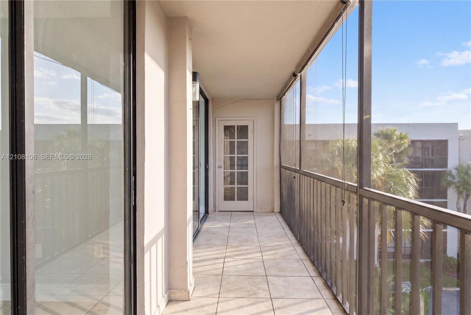 Covered balcony featuring tile flooring, full-height screening, metal railing, and glass-paneled door