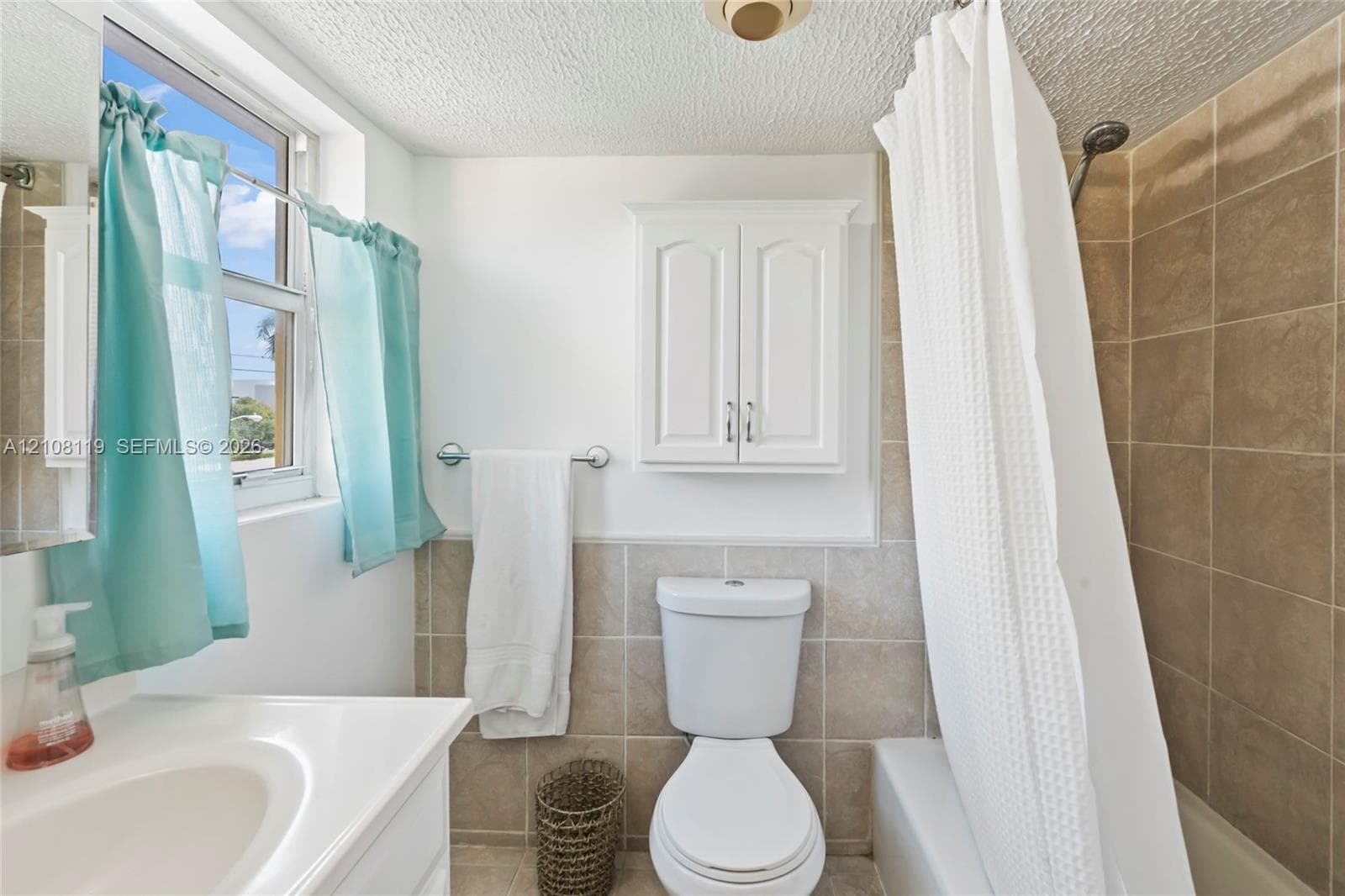 Bathroom featuring neutral tile wainscoting, a wall-mounted storage cabinet, an integrated vanity sink, and a combination tub and shower