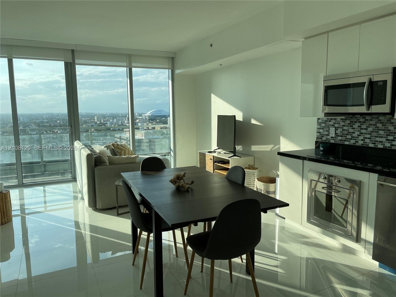 Floor-to-ceiling windows, high-gloss white cabinetry, mosaic tile backsplash, stainless steel appliances, and polished tile flooring