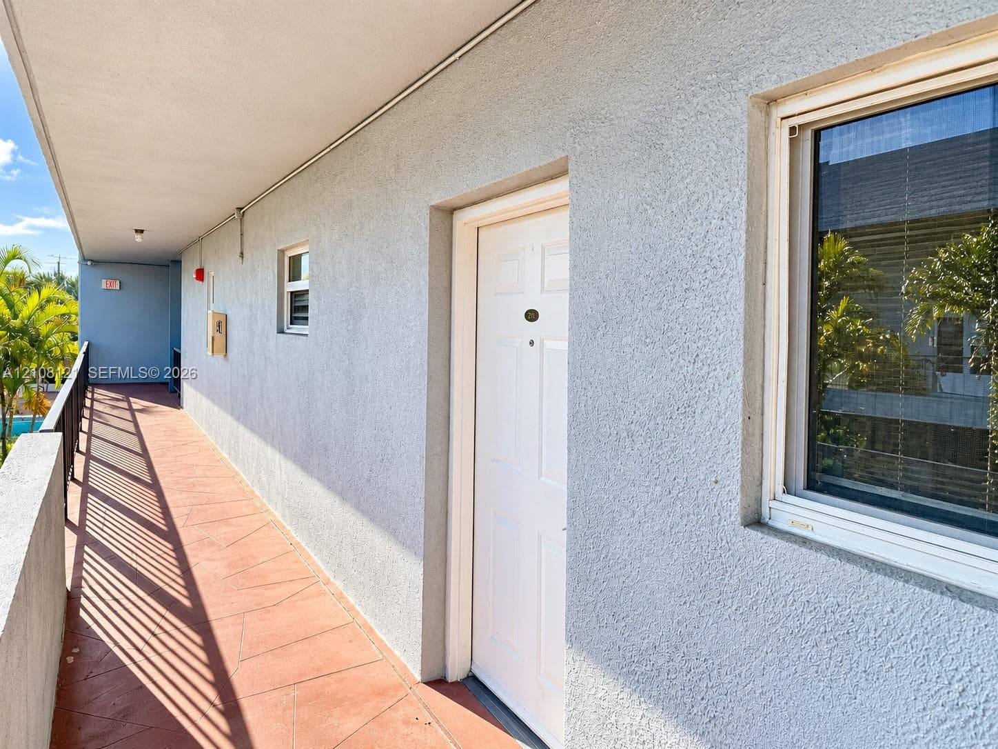 Exterior corridor featuring stucco wall finish, tiled flooring, metal railing, and multi-panel entry door