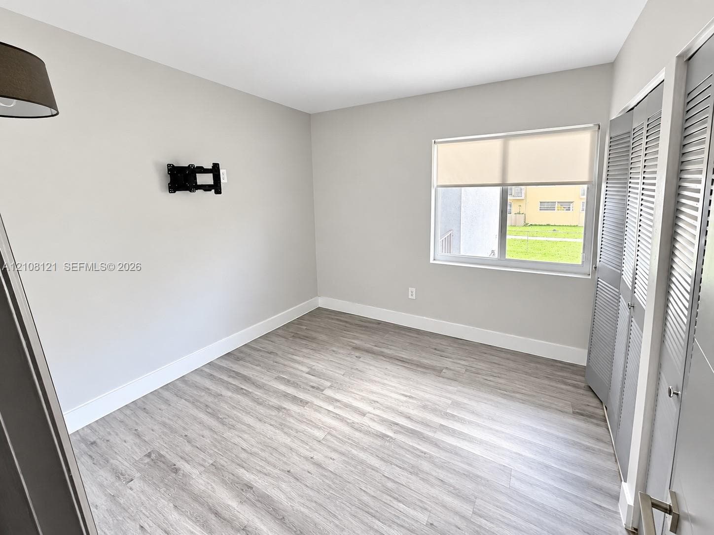 Room featuring wood-finish flooring, neutral wall paint, a sliding window with a roller shade, and bifold closet doors