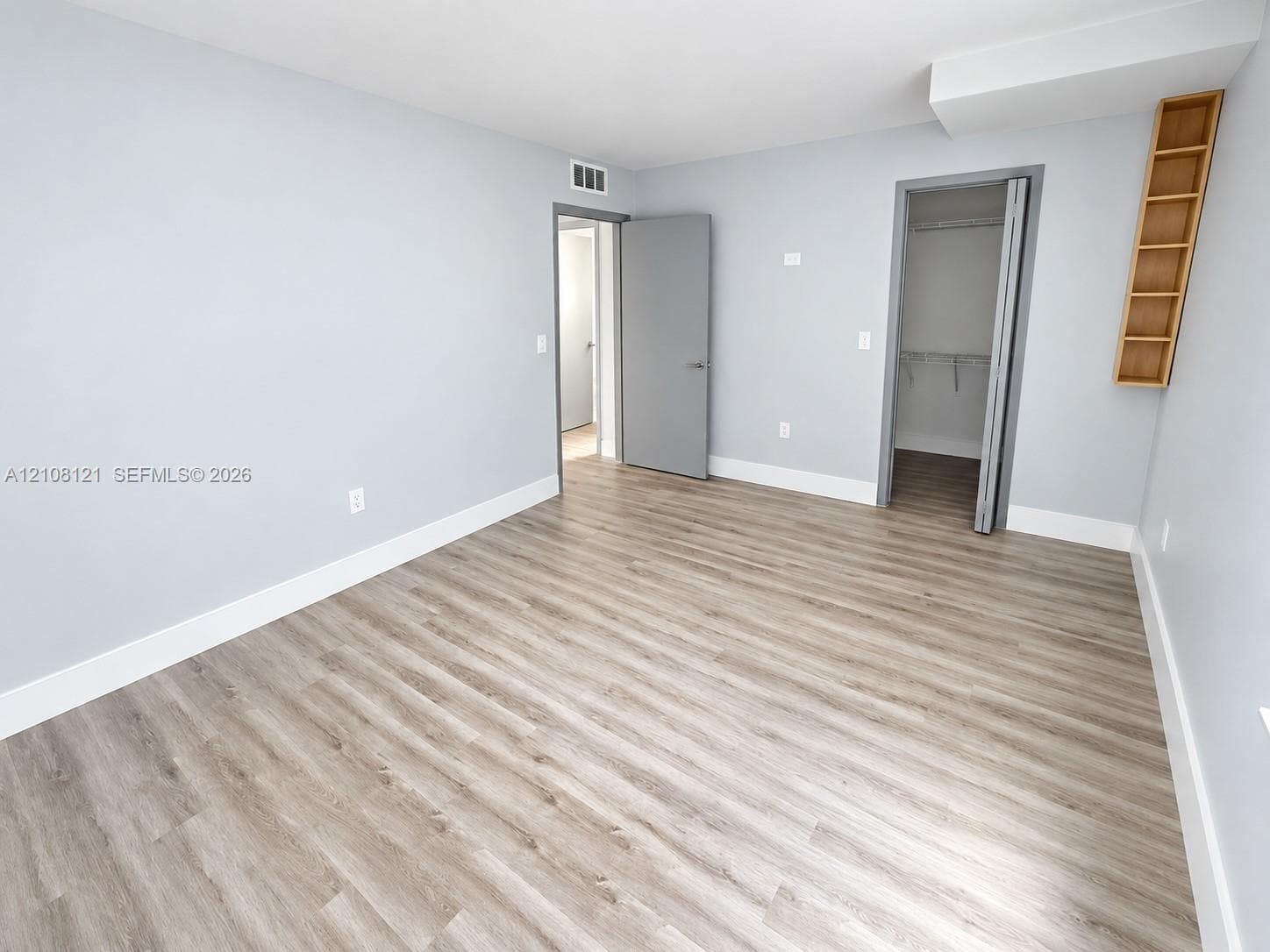 Wood-finish flooring, neutral wall tones, built-in wall shelving, and a walk-in closet with integrated wire storage