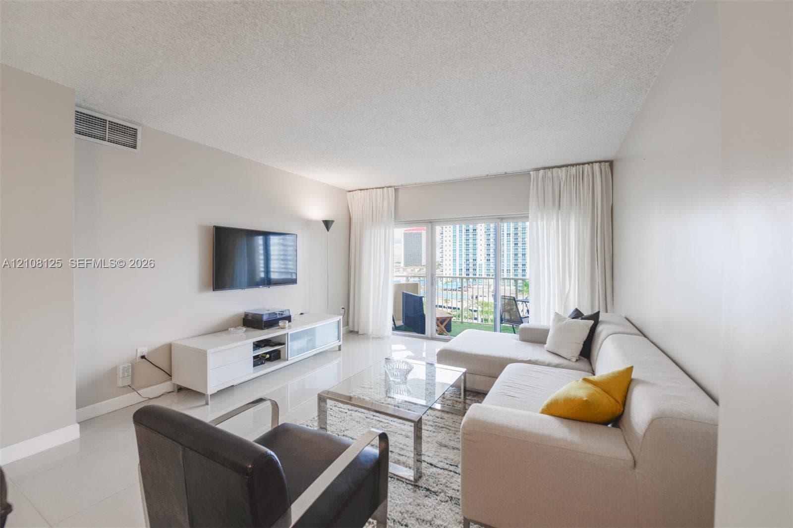 Living area featuring large-format tile flooring, textured ceiling, and sliding glass doors with access to a private balcony