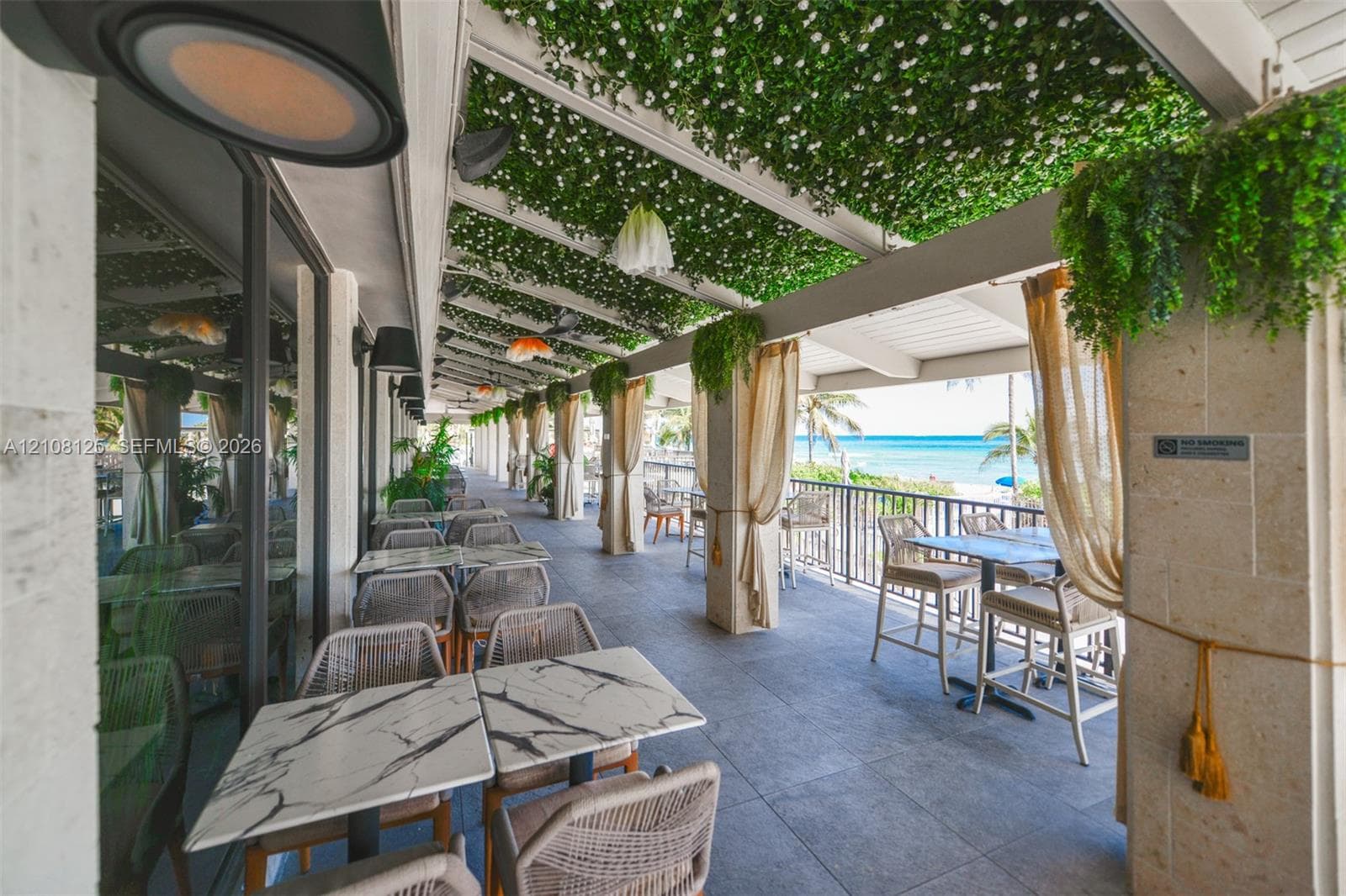 Covered outdoor patio featuring stone tile flooring, a pergola roof with integrated greenery, natural stone support columns, and metal perimeter railing