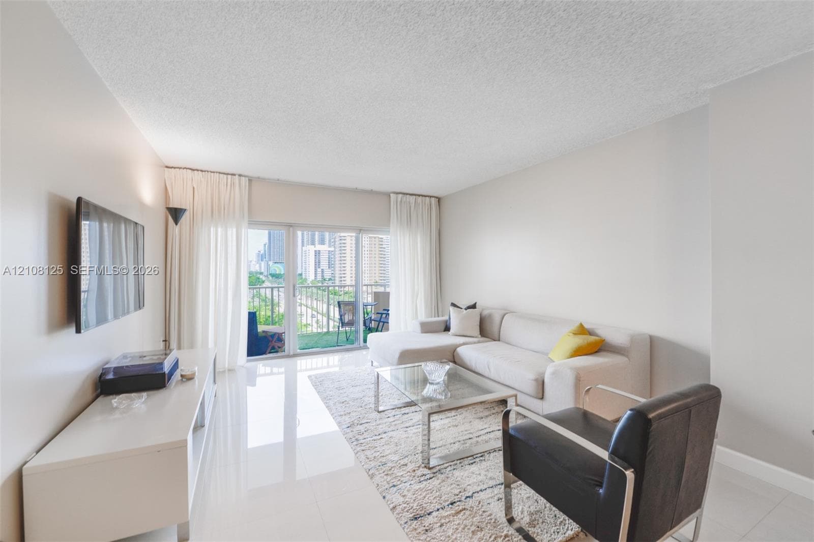 Living area featuring light-toned tile flooring, neutral wall paint, and floor-to-ceiling glass sliding doors providing access to an exterior balcony