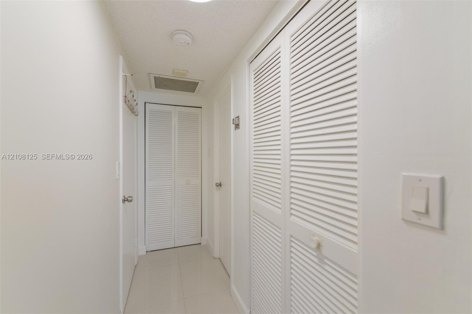 Hallway featuring high-gloss tile flooring, white-painted walls, and dual sets of white louvered-panel closet doors
