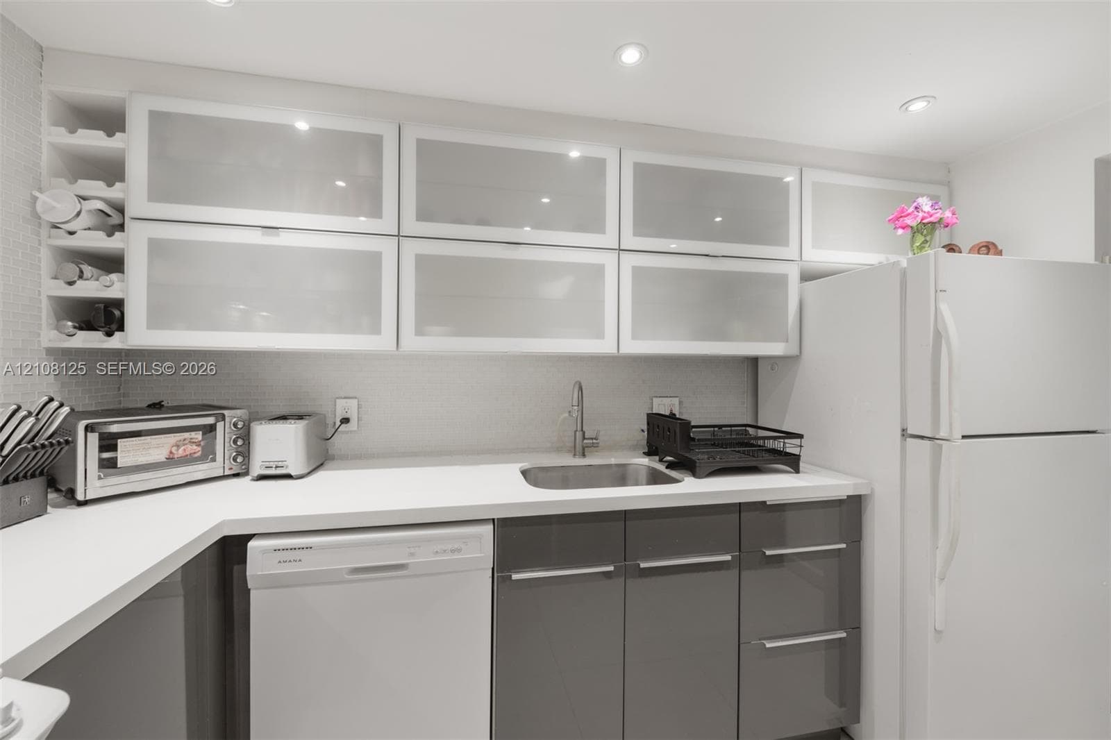 Kitchen featuring high-gloss charcoal base cabinetry, upper cabinets with frosted glass inserts, solid-surface countertops, recessed ceiling lighting, and integrated wine storage