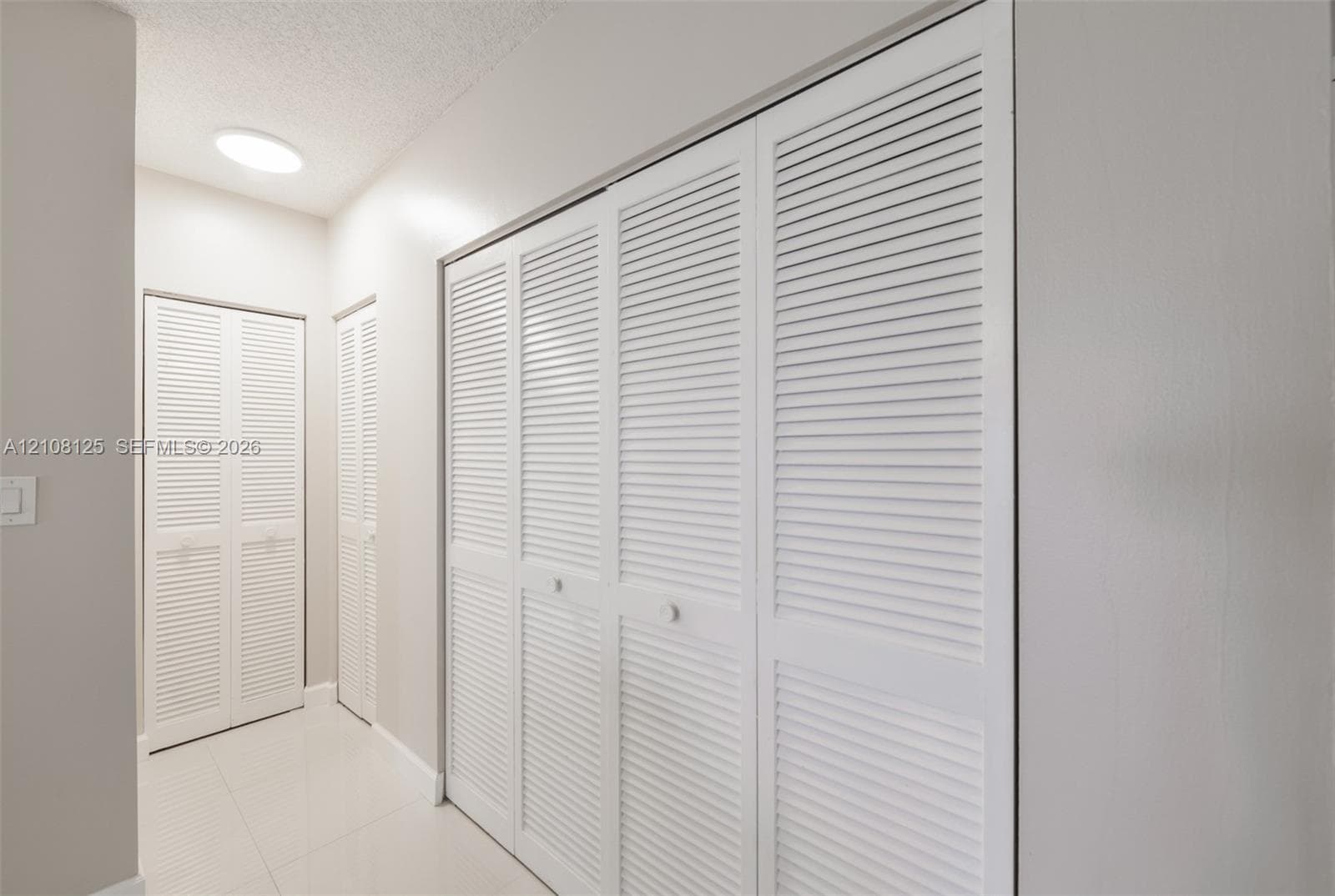 White louvered closet doors, neutral wall finish, and tile flooring