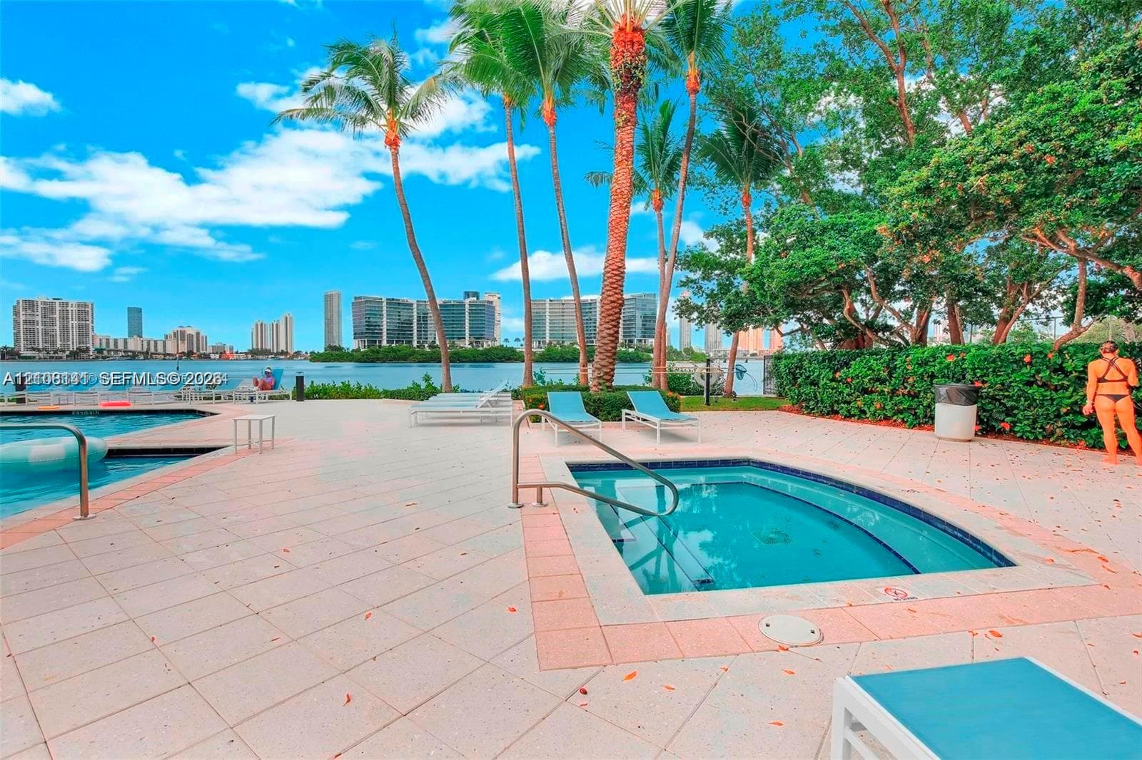 Waterfront pool and spa area featuring paved decking, mature palm trees, and metallic safety railings