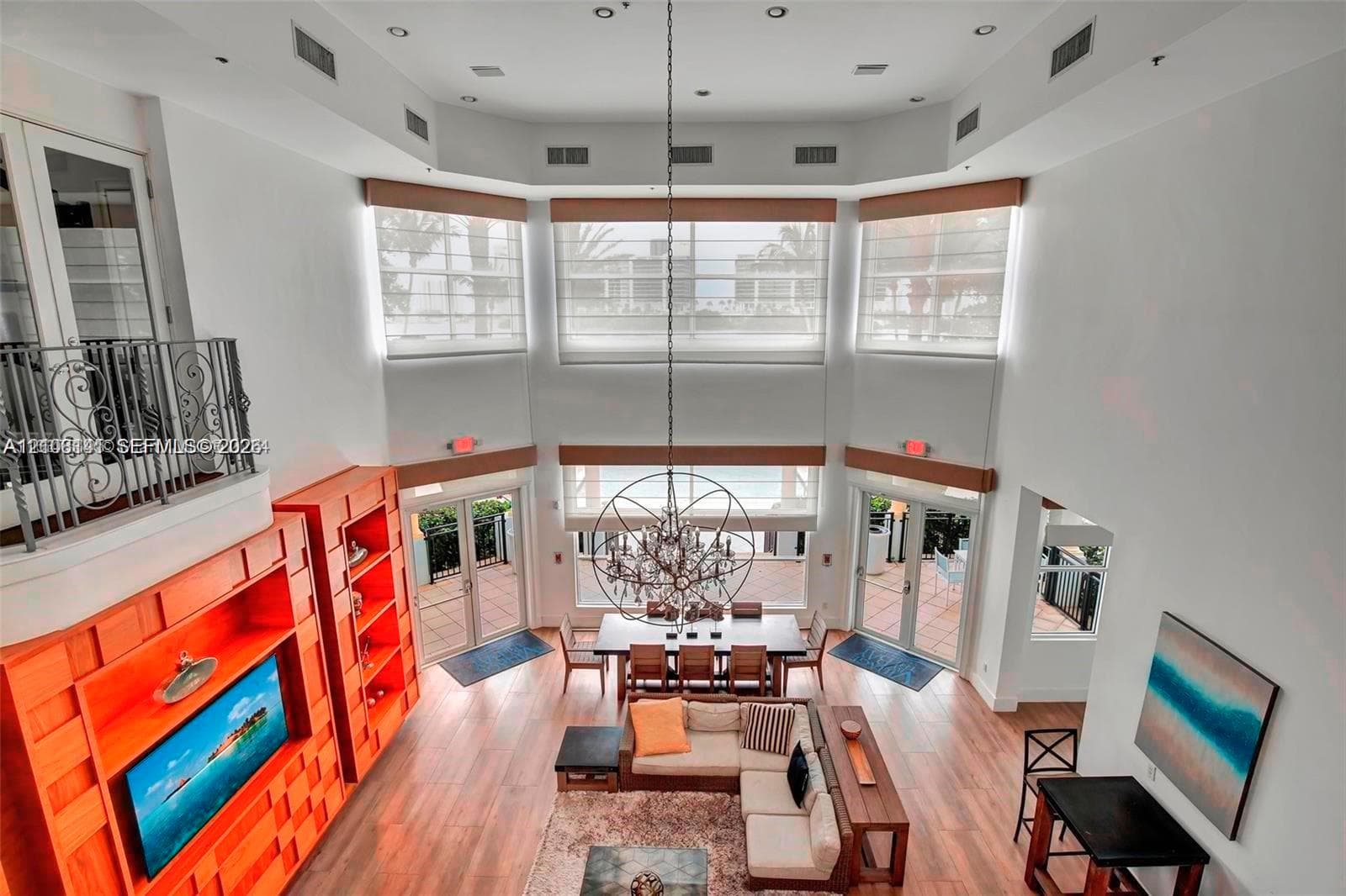 Double-height ceiling, floor-to-ceiling windows, custom built-in wood cabinetry, wood-finish flooring, and multi-tier spherical chandelier