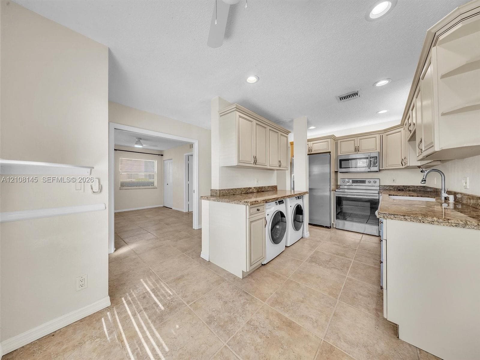 Kitchen featuring light-toned cabinetry, stone-finish countertops, stainless steel appliances, integrated laundry area, and tile flooring
