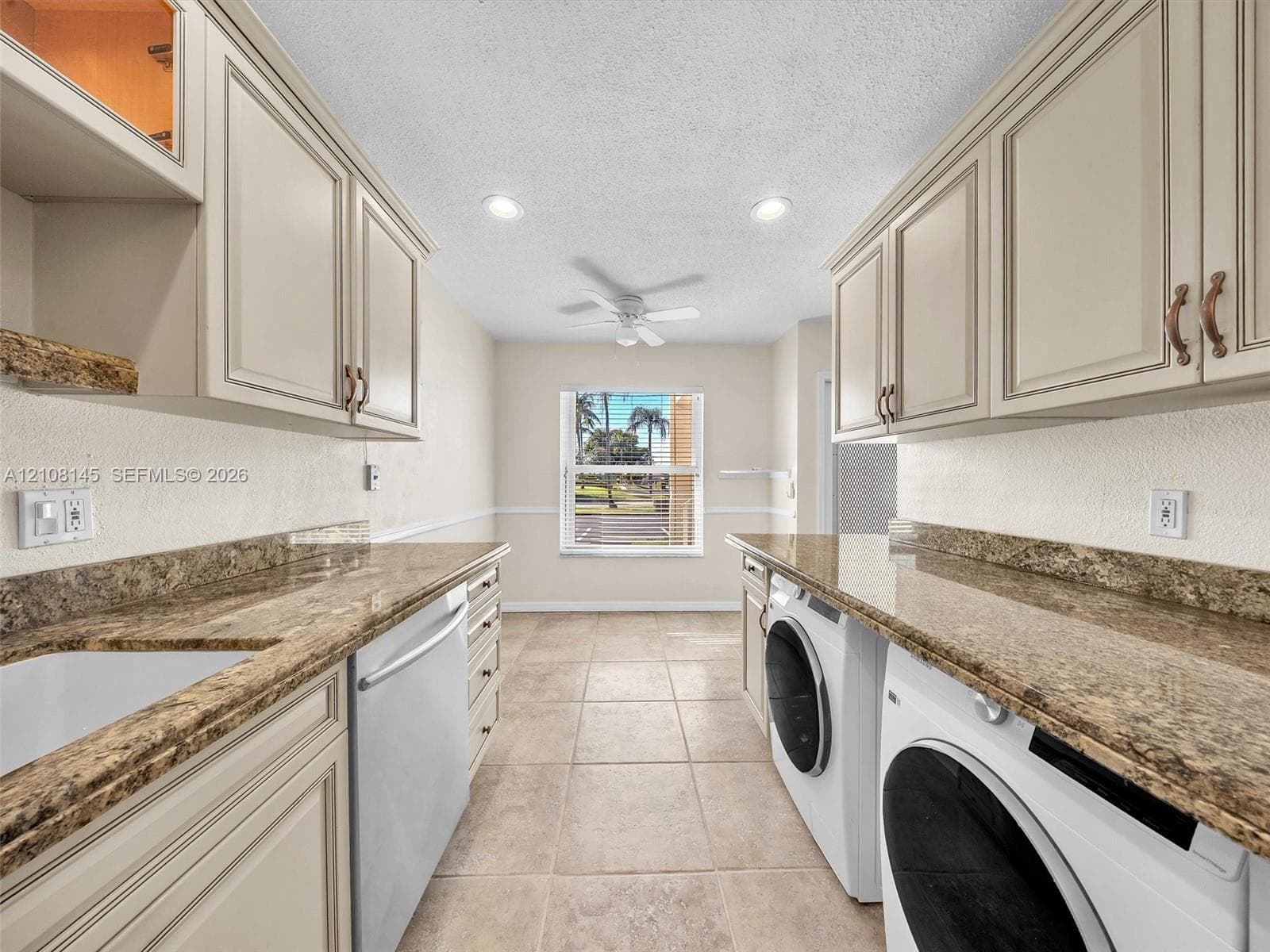 Laundry room featuring custom cabinetry, stone-finish countertops, tile flooring, recessed lighting, and a white basin sink