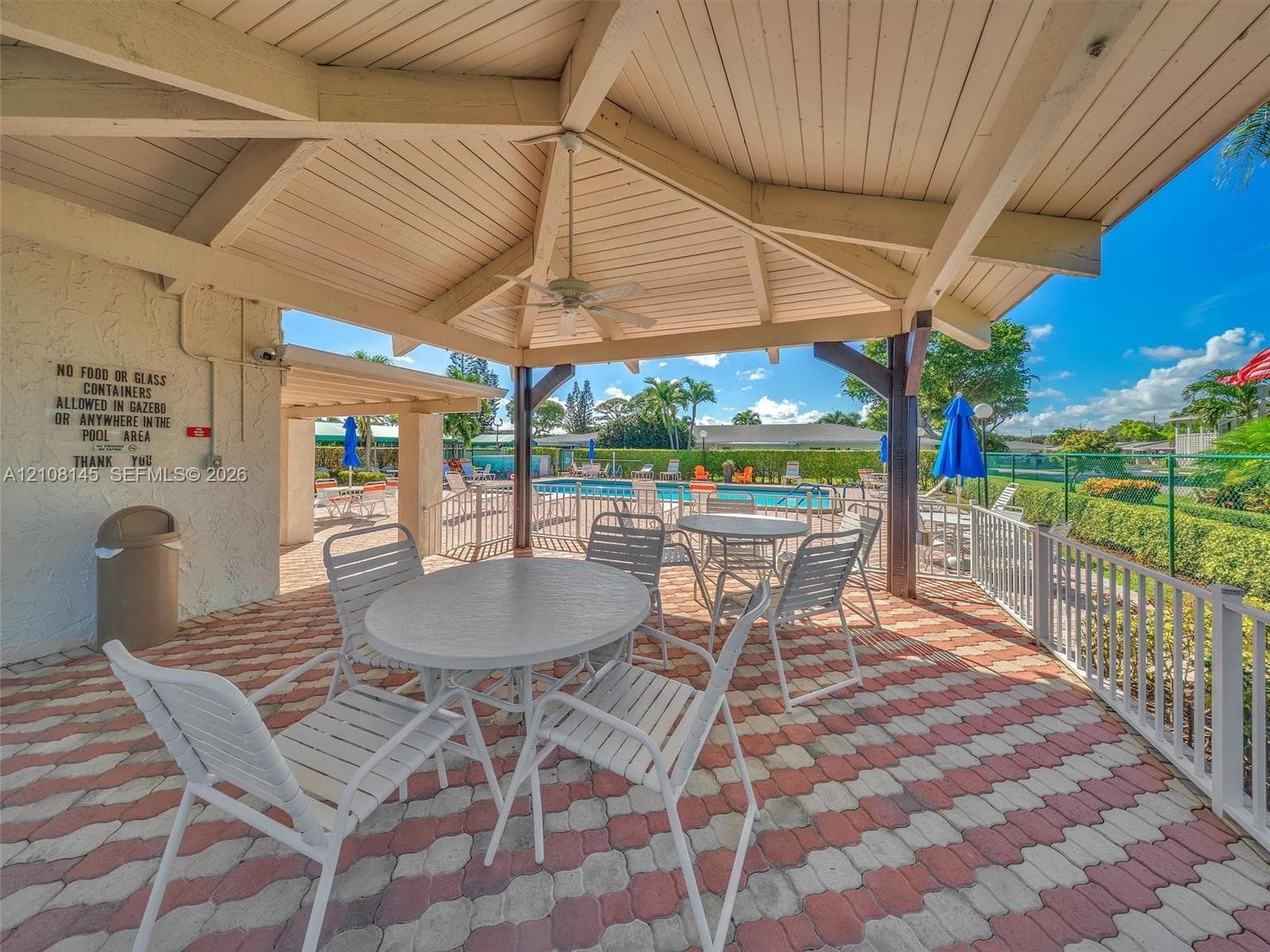 Covered outdoor gazebo featuring a vaulted wood-beam ceiling, ceiling fan, and decorative brick paver flooring