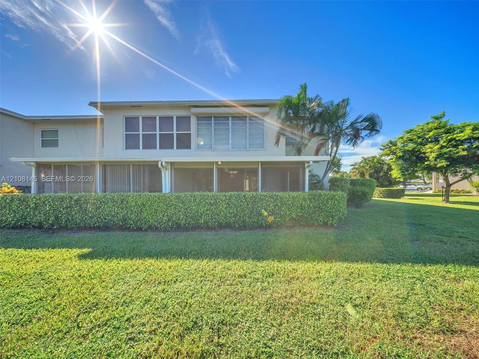 Two-story exterior featuring a screened-in ground-level patio, multi-pane windows, mature landscaping, and an expansive lawn