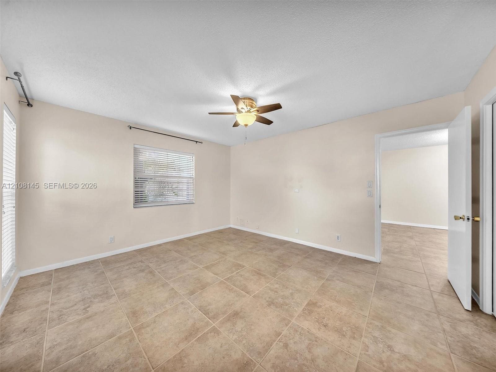 Neutral-toned interior space featuring large-format stone-style tile flooring, dual windows with horizontal blinds, and a central ceiling fan with integrated light fixture