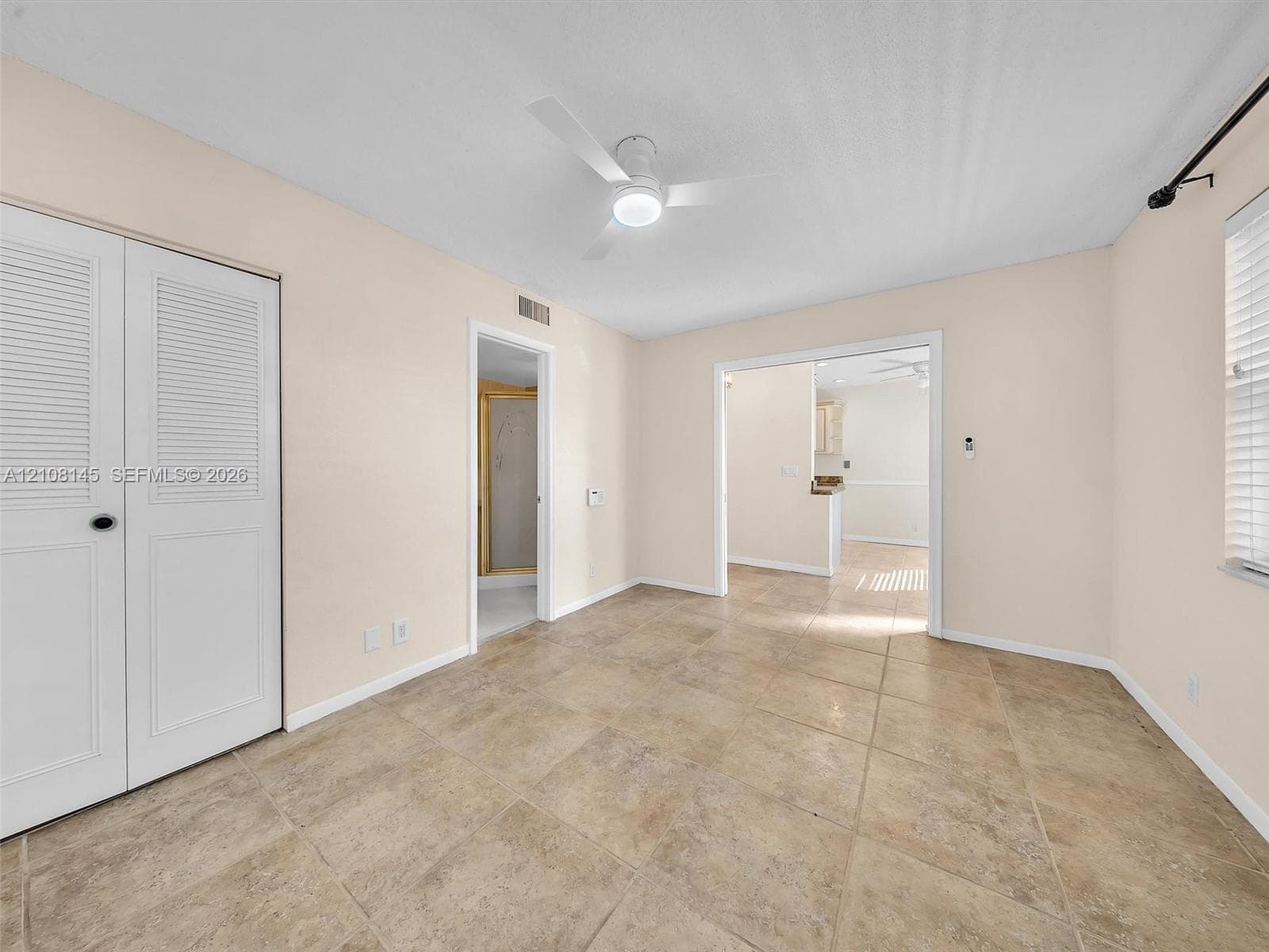 Interior space featuring large-format ceramic tile flooring, neutral wall tones, a ceiling-mounted light fixture with fan, and double-door closet storage