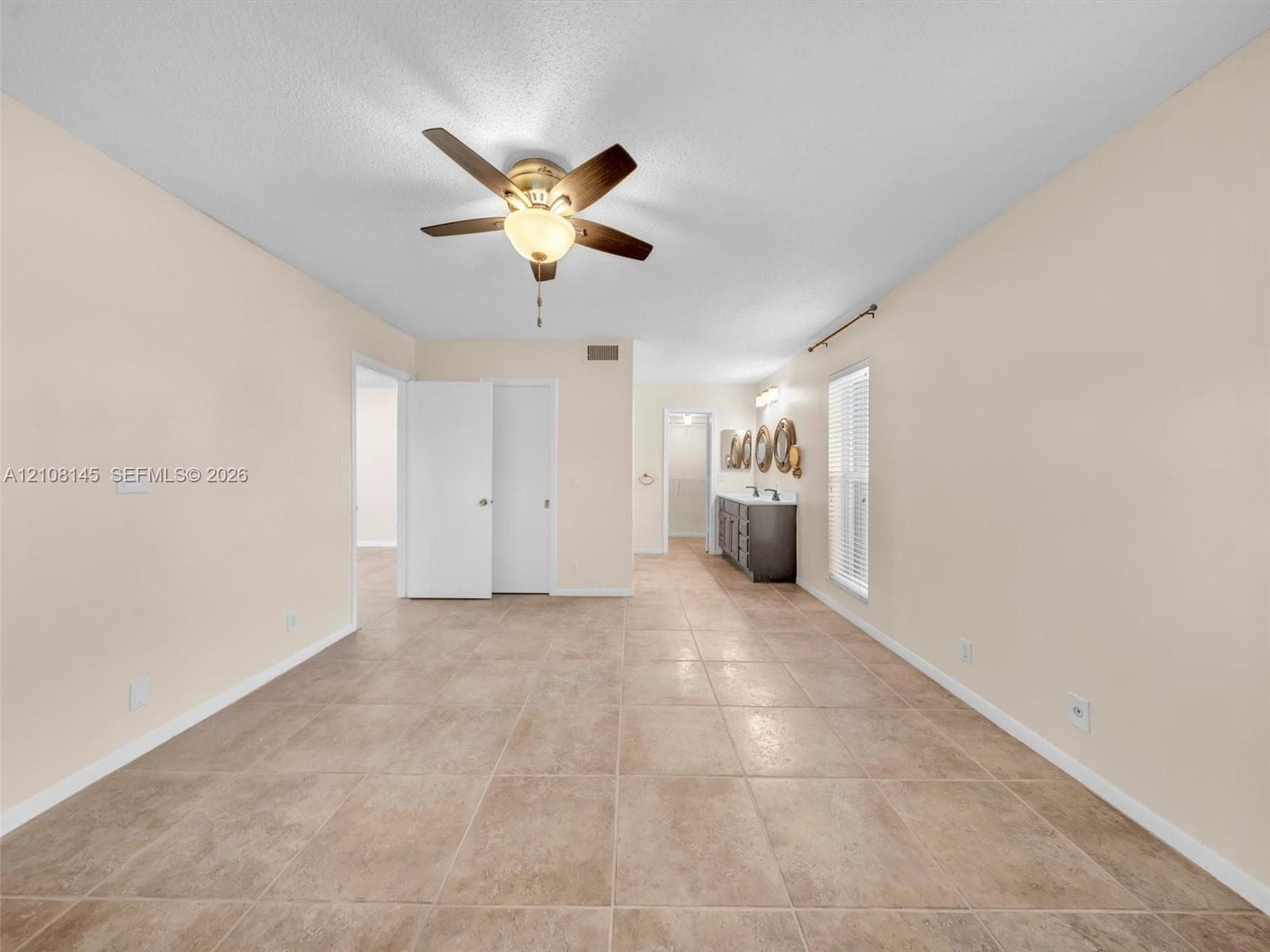 Large-format tile flooring, ceiling fan with integrated light fixture, dual-sink vanity with stone-surface countertop, and window blinds
