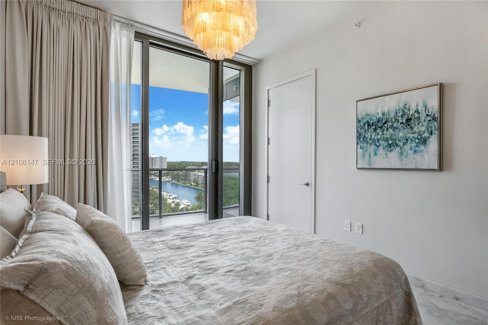 Floor-to-ceiling glass sliding doors opening to a balcony, polished stone-finish flooring, and a multi-tiered tiered chandelier