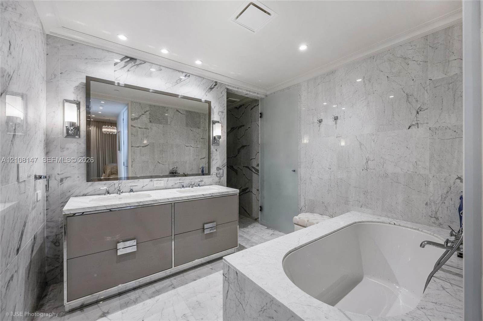 Dual-sink vanity with high-gloss cabinetry, stone-surround soaking tub, wall-to-wall stone tiling, and recessed lighting