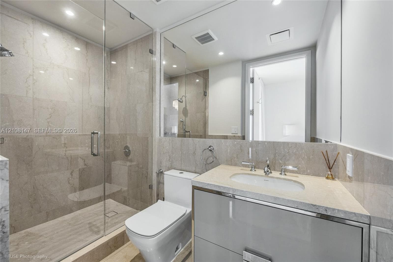 Glass-enclosed walk-in shower with floor-to-ceiling tile, high-gloss vanity with stone countertop, undermount sink, and full-width wall mirror