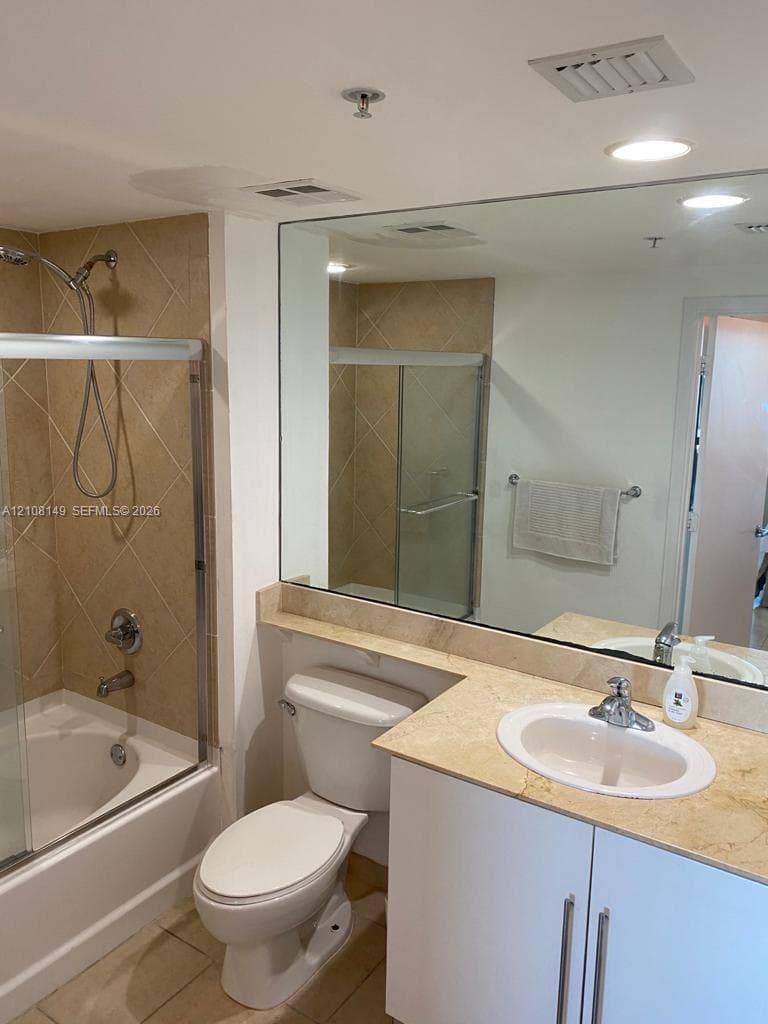 Bathroom featuring a full-width vanity mirror, stone-surface countertop, integrated white cabinetry, and a tub-shower combination with full-height tile surround