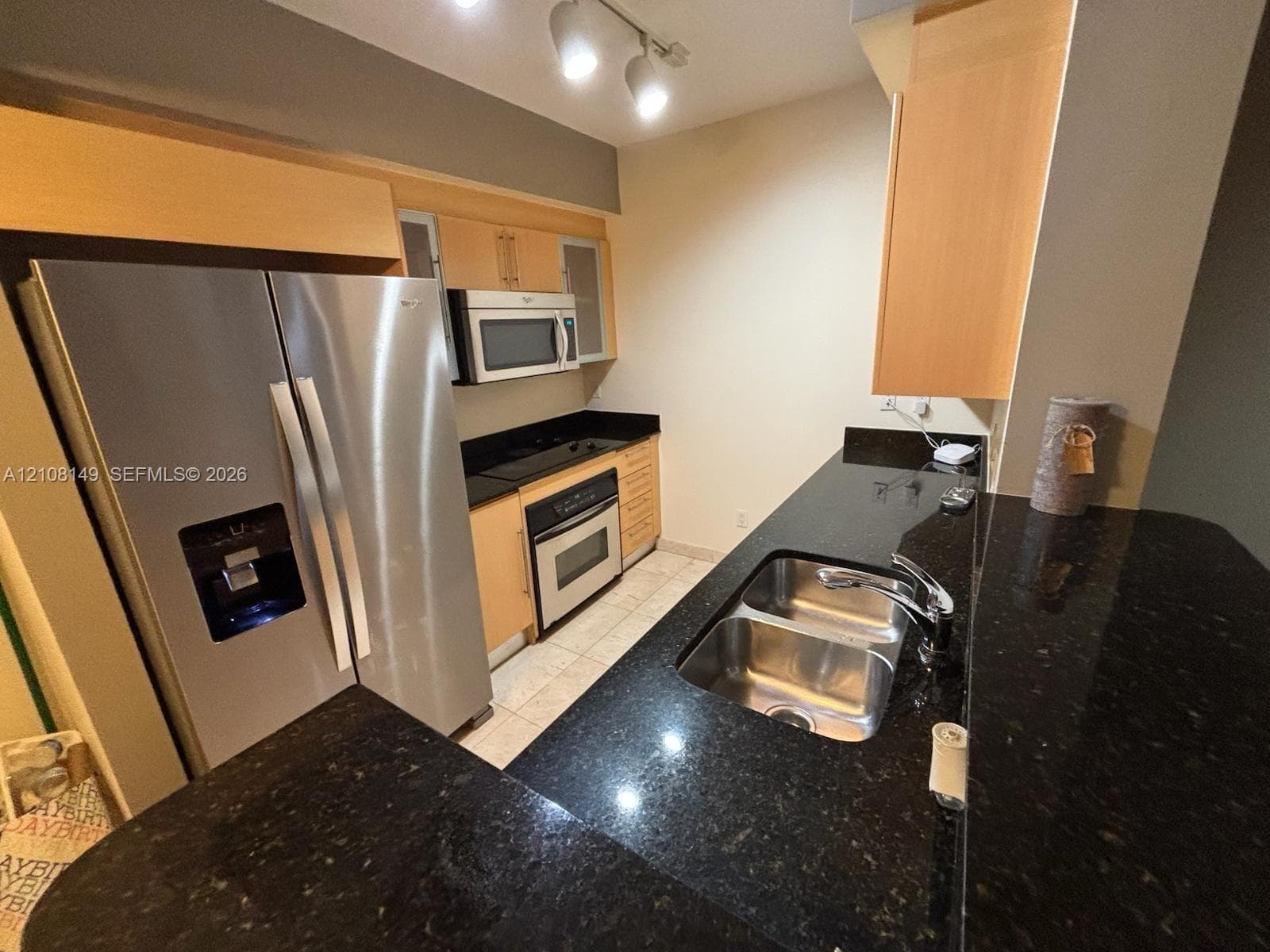 Kitchen featuring light wood cabinetry, dark stone countertops, stainless steel appliances, a double-basin undermount sink, and track lighting