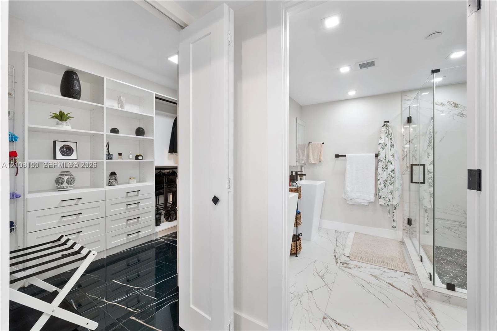 Walk-in closet featuring white built-in shelving and drawer cabinetry, complemented by high-gloss dark stone-finish flooring