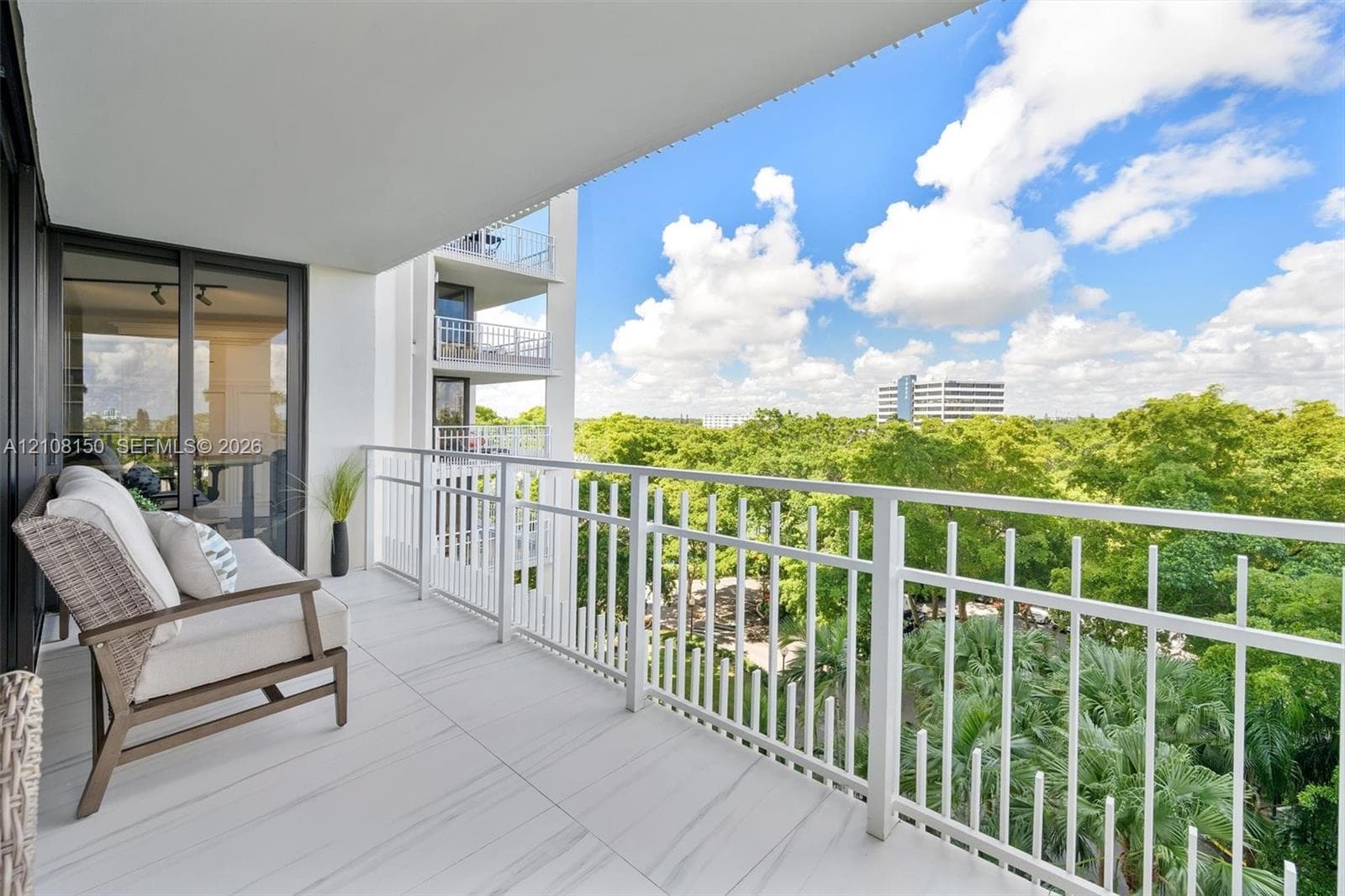 Covered balcony featuring white tile flooring, white metal railing, and sliding glass entry doors