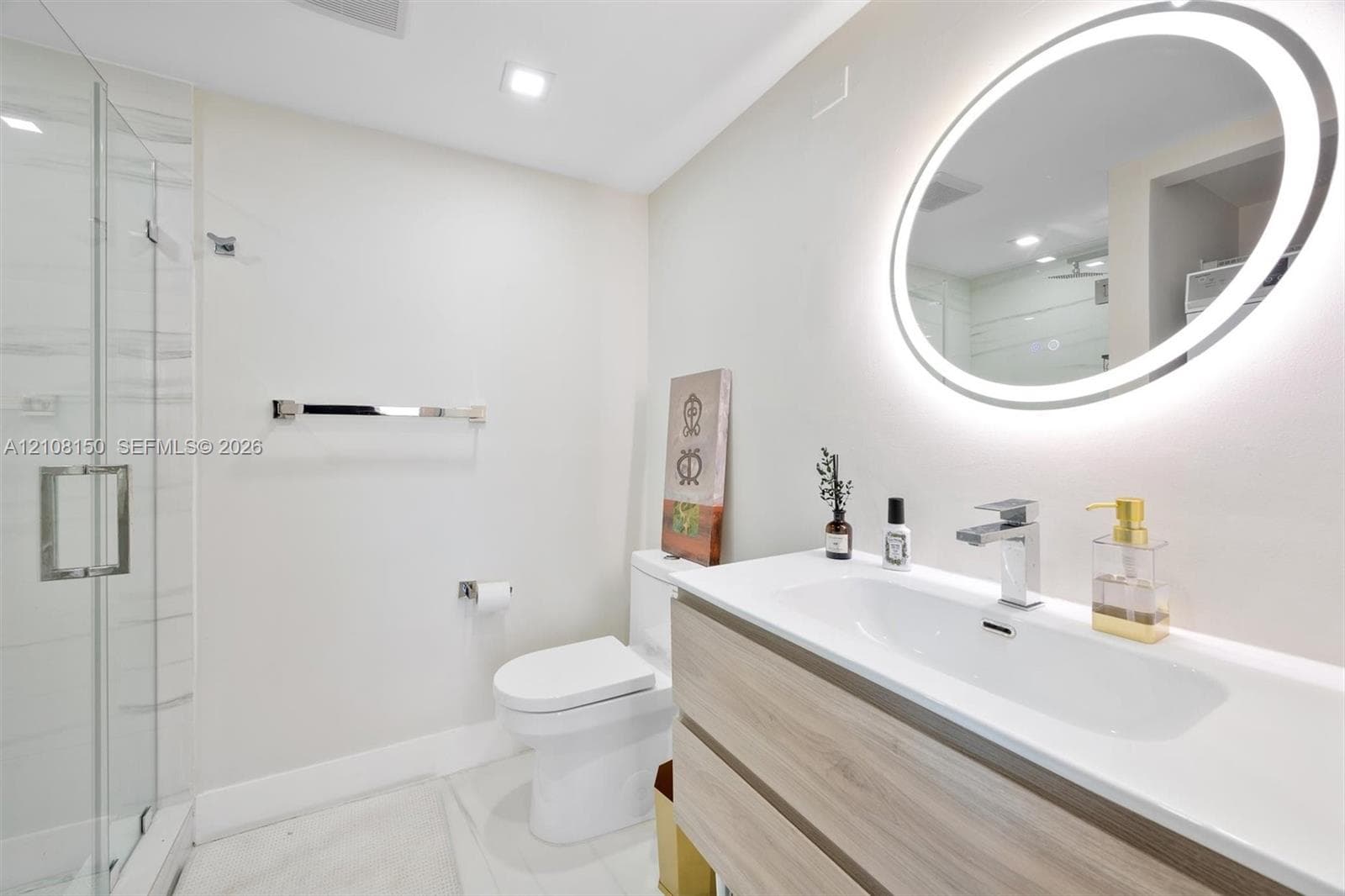 Bathroom featuring a wall-mounted vanity with wood-finish cabinetry, an integrated sink with a chrome faucet, a backlit oval mirror, and a walk-in glass shower enclosure