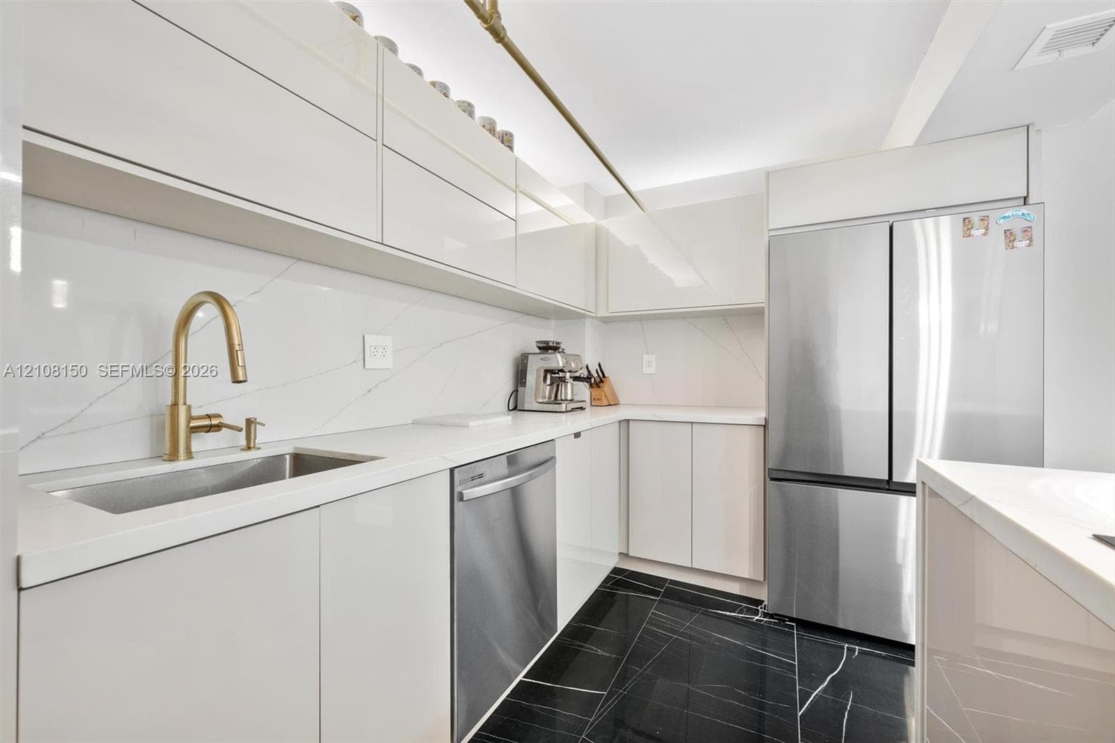 Kitchen featuring high-gloss cabinetry, stone-surface countertops, full-height stone backsplash, stainless steel appliances, and dark-toned flooring with light veining